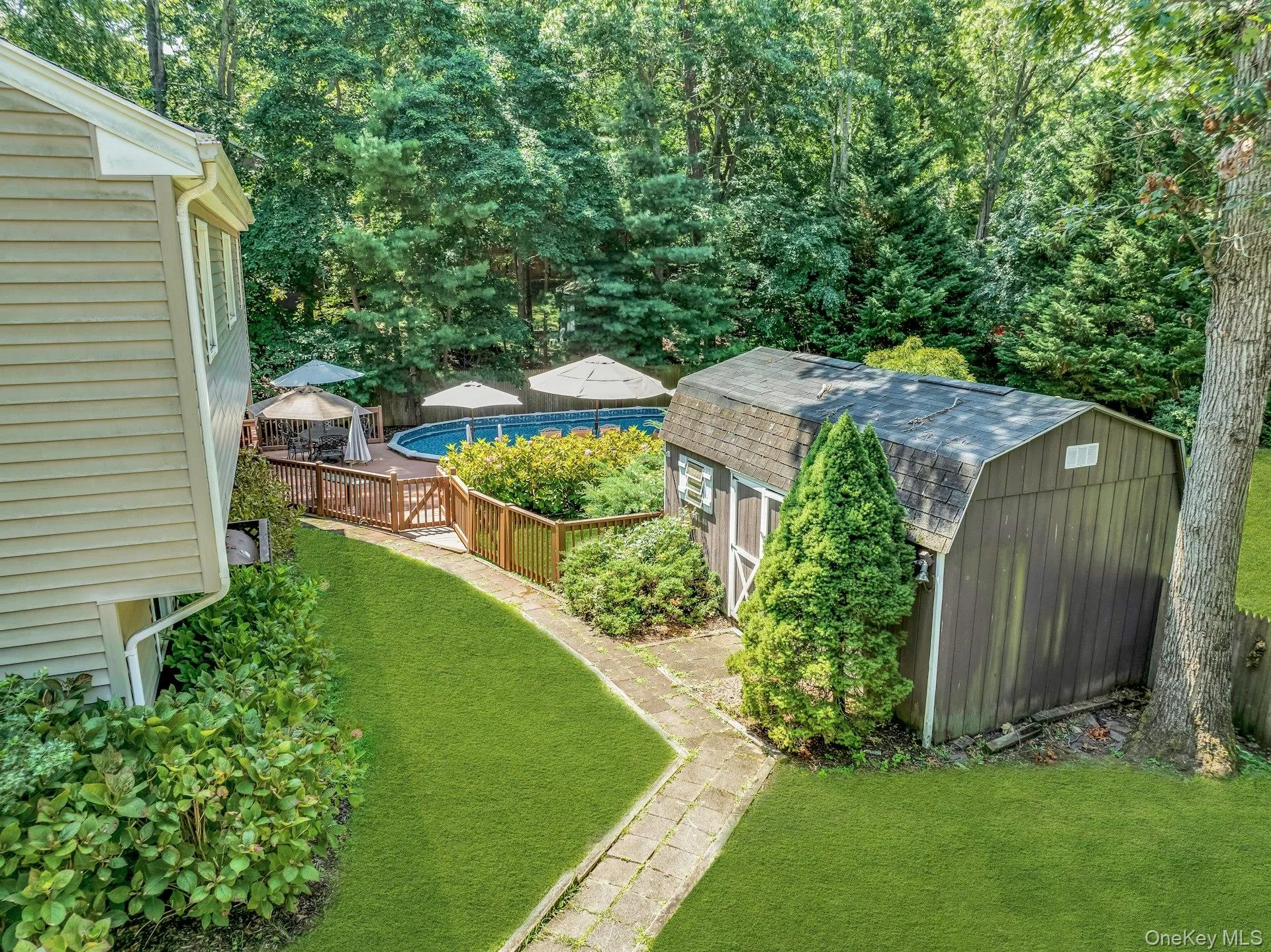 Expansive backyard oasis featuring a professionally manicured lawn, mature tree canopy, stone-paved pathway, in-ground swimming pool with wooden deck, and multiple outbuildings including storage sheds Expansive backyard oasis featuring a professionally manicured lawn, mature tree canopy, stone-paved pathway, in-ground swimming pool with wooden deck, and multiple outbuildings including storage sheds