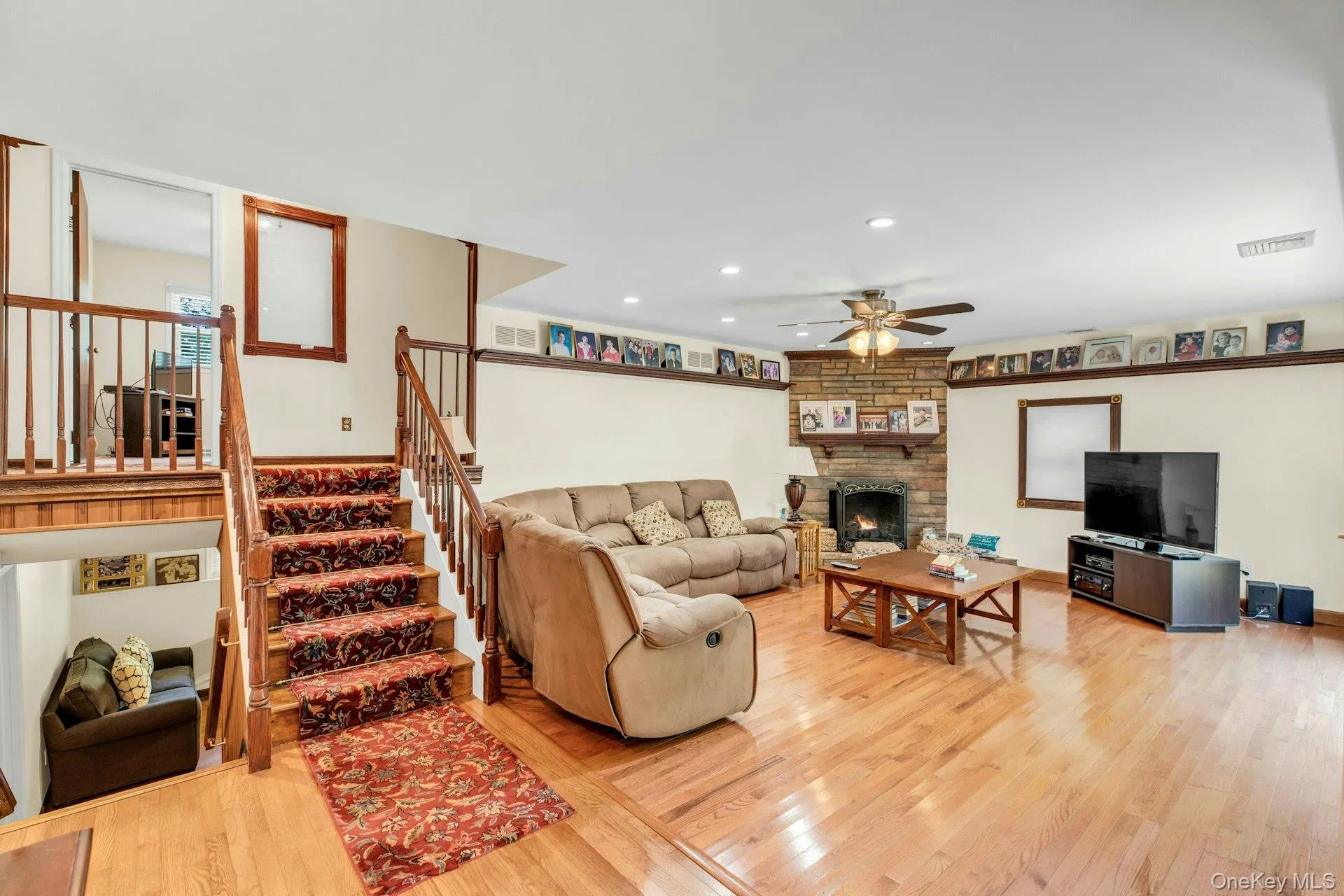 Open-concept living space featuring hardwood flooring, a wood-burning fireplace with surround, and multiple seating areas Open-concept living space featuring hardwood flooring, a wood-burning fireplace with surround, and multiple seating areas