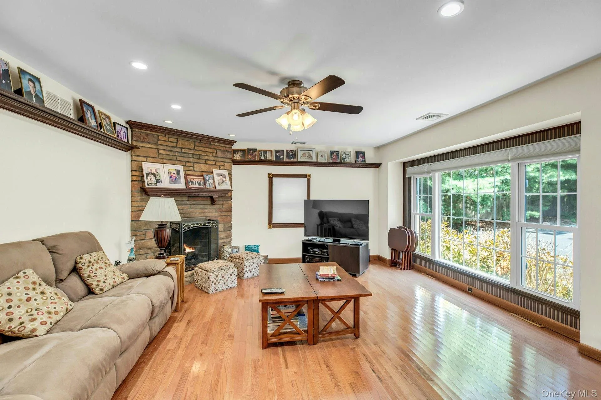 Living area featuring hardwood flooring, a stone-front fireplace with mantel, recessed lighting, and a ceiling fan Living area featuring hardwood flooring, a stone-front fireplace with mantel, recessed lighting, and a ceiling fan