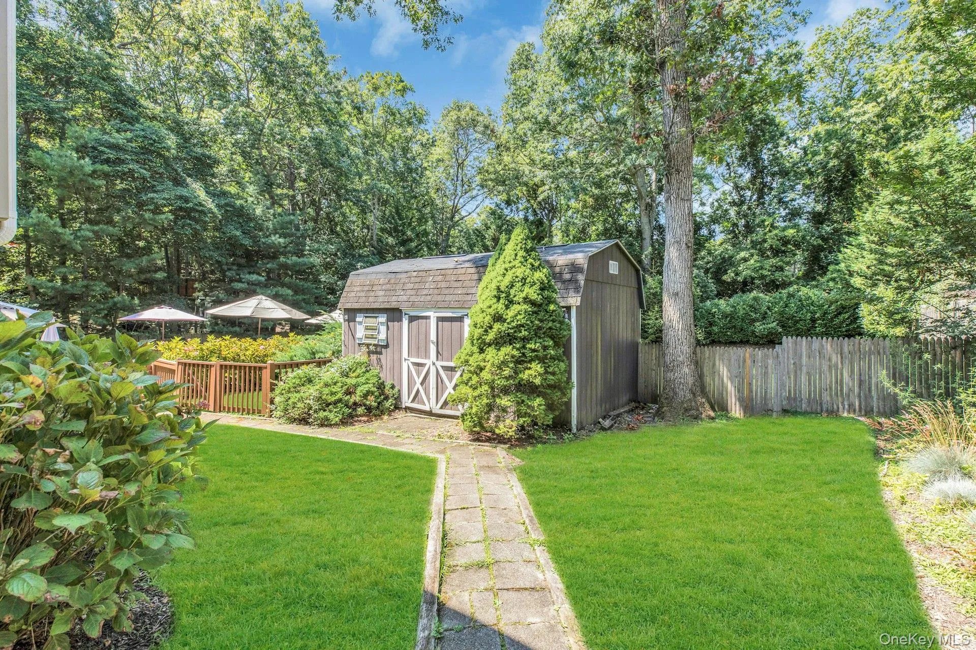 Expansive backyard oasis featuring a meticulously manicured lawn, mature tree-lined perimeter, and charming detached storage shed with X-brace detailing Expansive backyard oasis featuring a meticulously manicured lawn, mature tree-lined perimeter, and charming detached storage shed with X-brace detailing