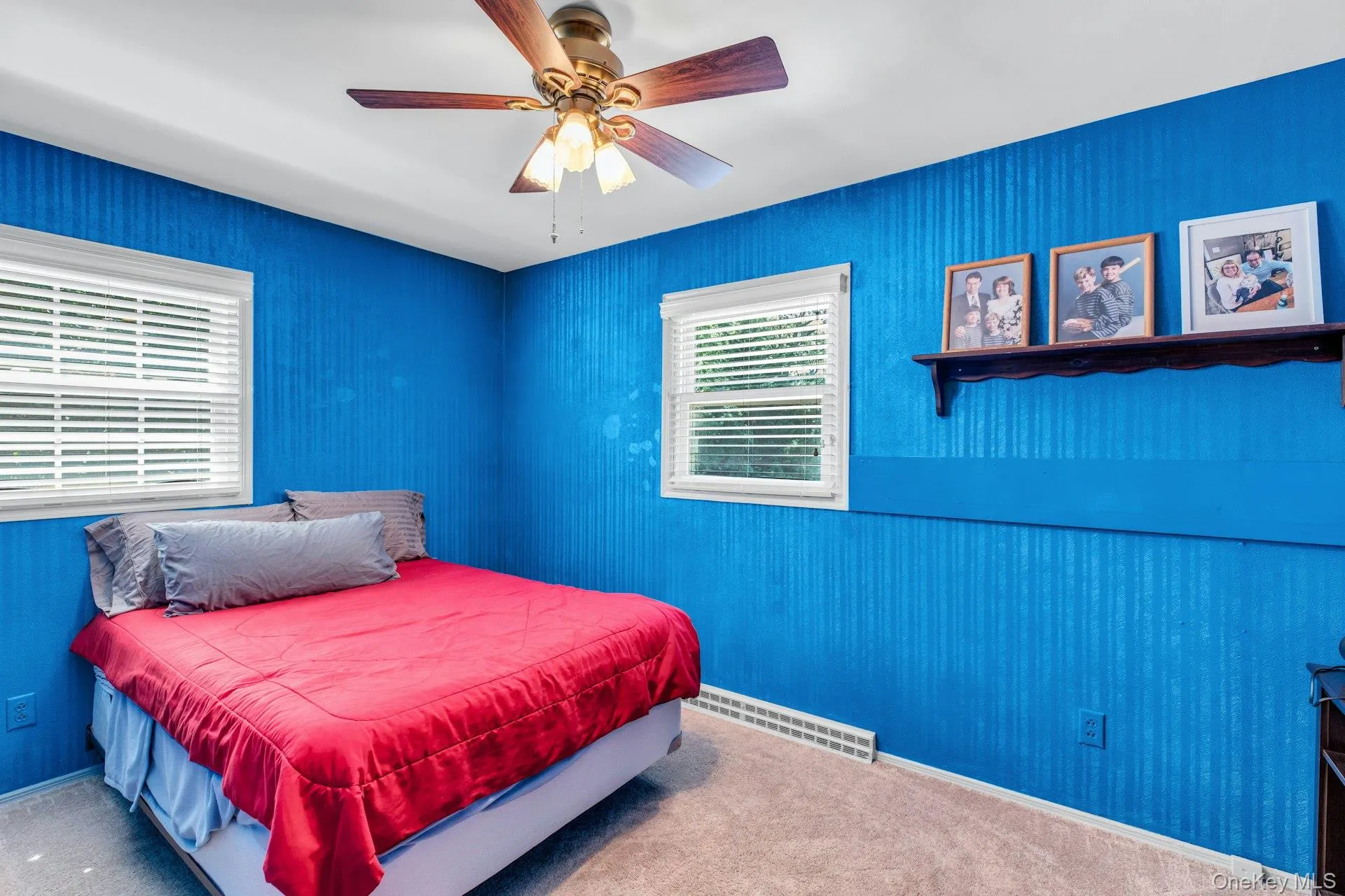 Bright bedroom retreat showcasing vibrant blue textured wall paneling, carpeted flooring, and dual casement windows with plantation shutters Bright bedroom retreat showcasing vibrant blue textured wall paneling, carpeted flooring, and dual casement windows with plantation shutters