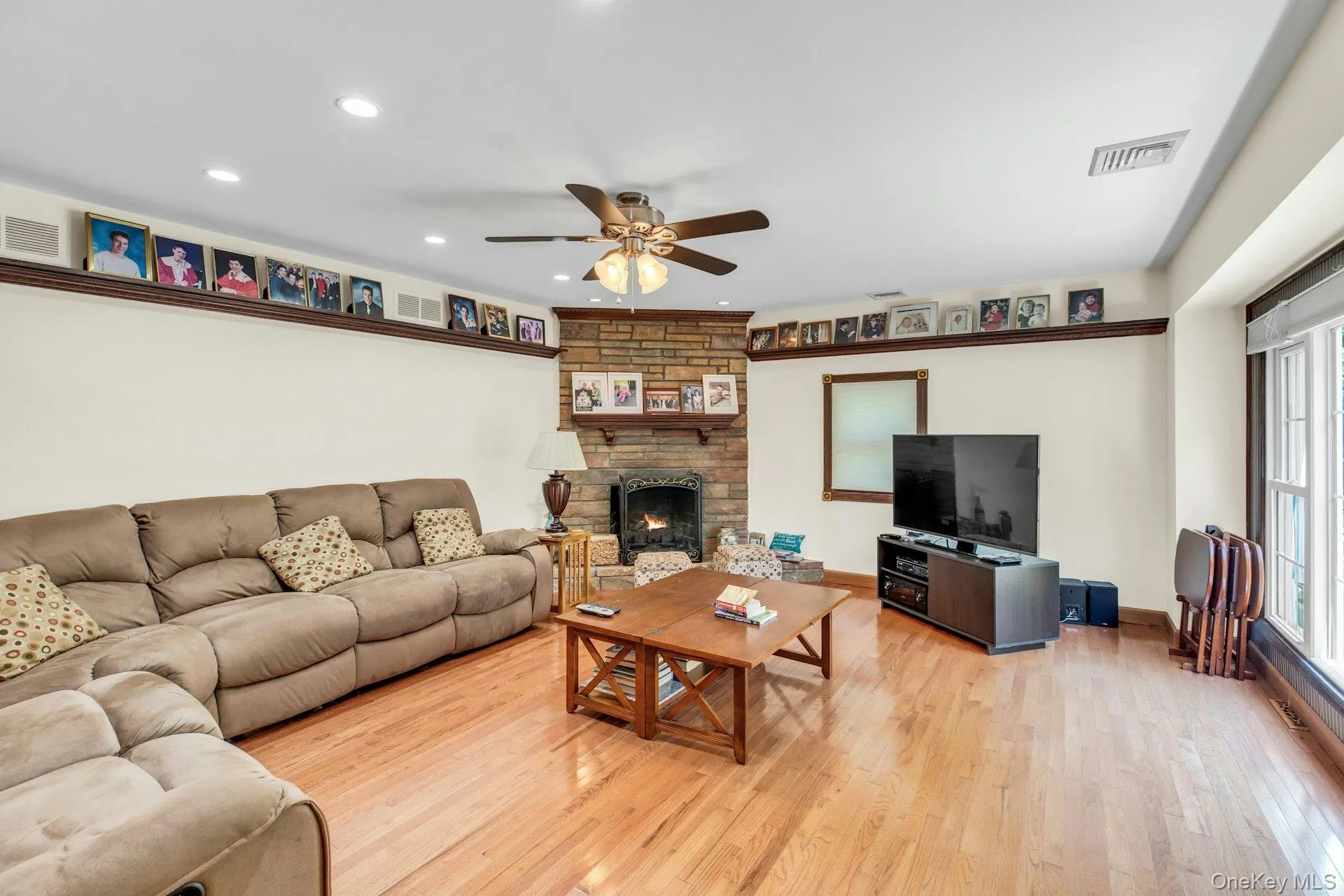 Living room featuring hardwood flooring, a stone-clad fireplace with mantel, recessed lighting, and a ceiling fan Living room featuring hardwood flooring, a stone-clad fireplace with mantel, recessed lighting, and a ceiling fan