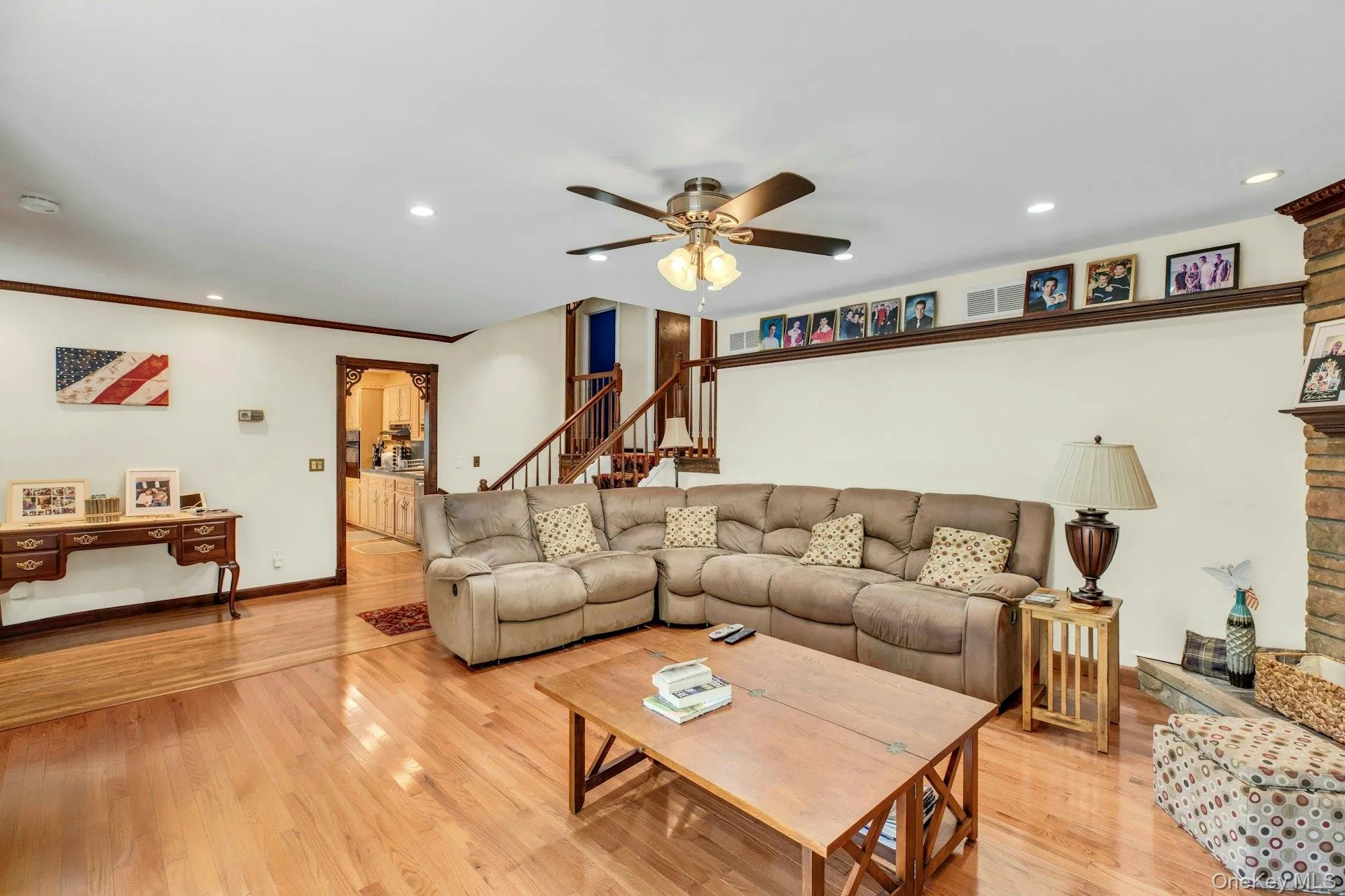 Spacious open-concept living area showcasing hardwood flooring, a neutral upholstered sectional sofa, coffered ceiling with ceiling fan, recessed lighting, and a wood-top coffee table Spacious open-concept living area showcasing hardwood flooring, a neutral upholstered sectional sofa, coffered ceiling with ceiling fan, recessed lighting, and a wood-top coffee table