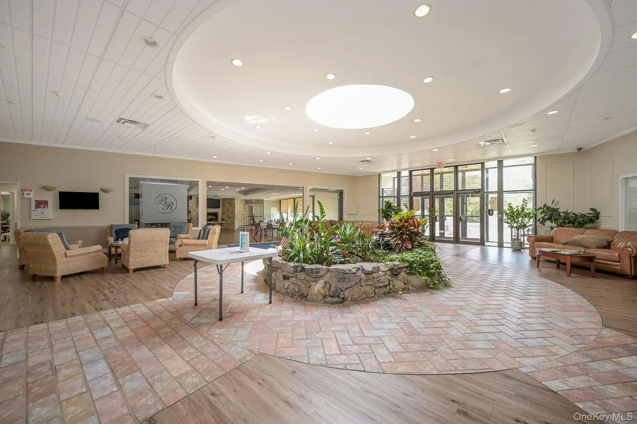 Expansive reception area featuring recessed lighting, a stone-edged planter, large glass entry doors, and a decorative ceiling with a central circular light fixture Expansive reception area featuring recessed lighting, a stone-edged planter, large glass entry doors, and a decorative ceiling with a central circular light fixture