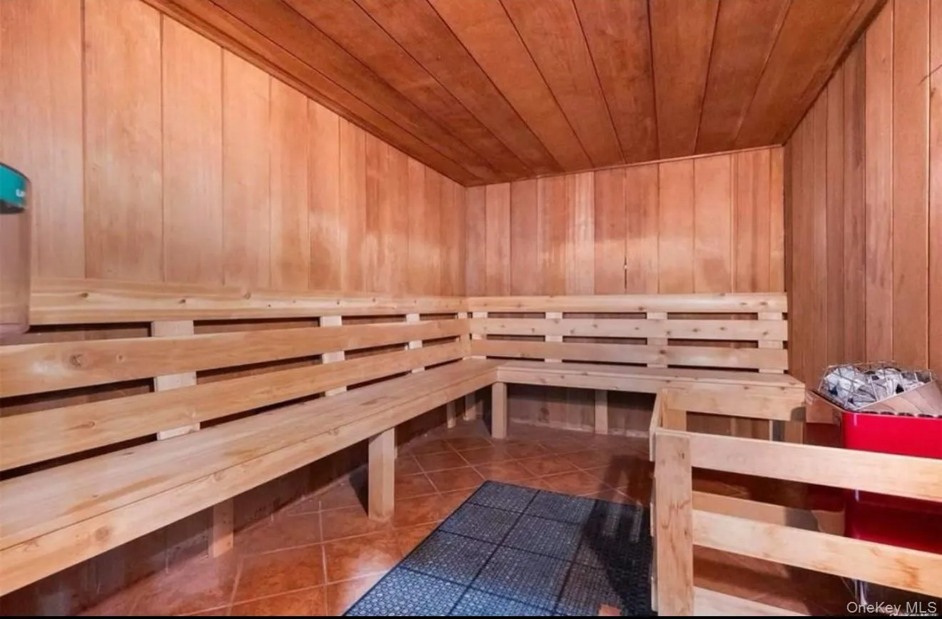 Sauna featuring tiered wood-finish benches with horizontal slat design, wood-paneled walls and ceiling, and dark tile flooring Sauna featuring tiered wood-finish benches with horizontal slat design, wood-paneled walls and ceiling, and dark tile flooring