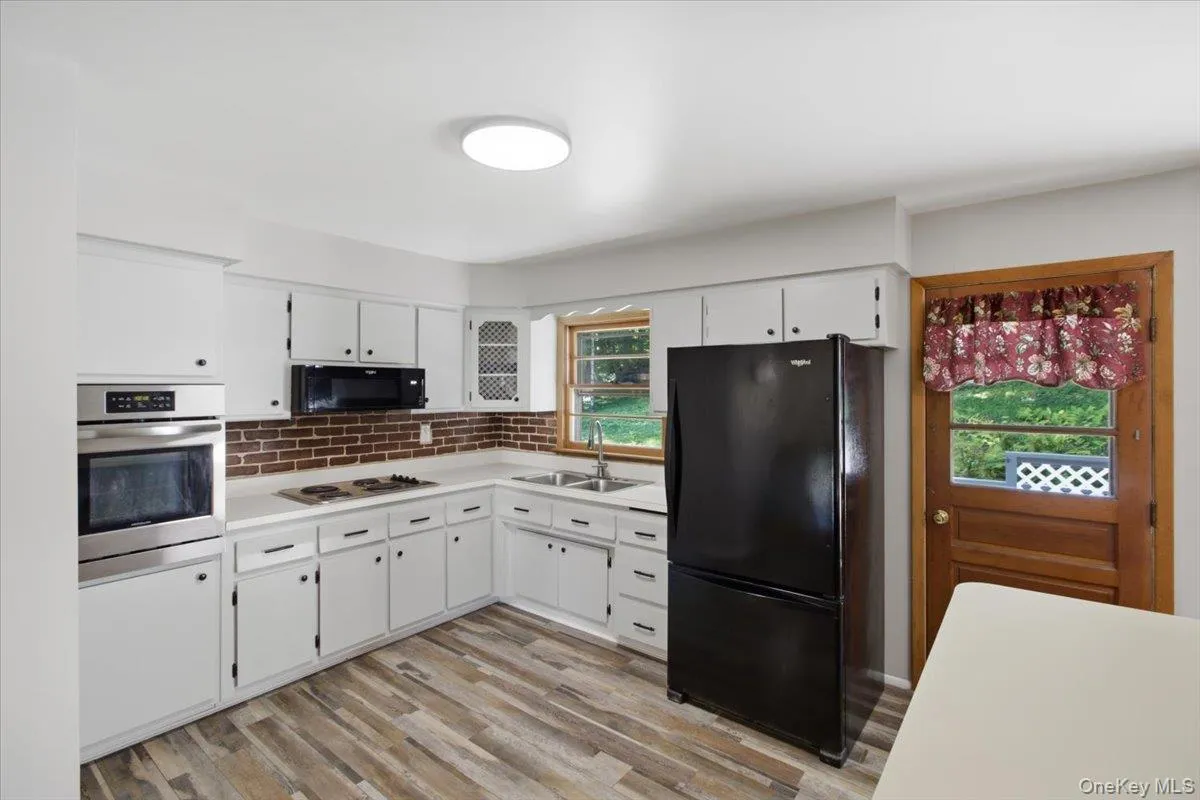 Kitchen featuring white cabinetry, brick-finish backsplash, wood-finish flooring, and stainless steel built-in oven Kitchen featuring white cabinetry, brick-finish backsplash, wood-finish flooring, and stainless steel built-in oven