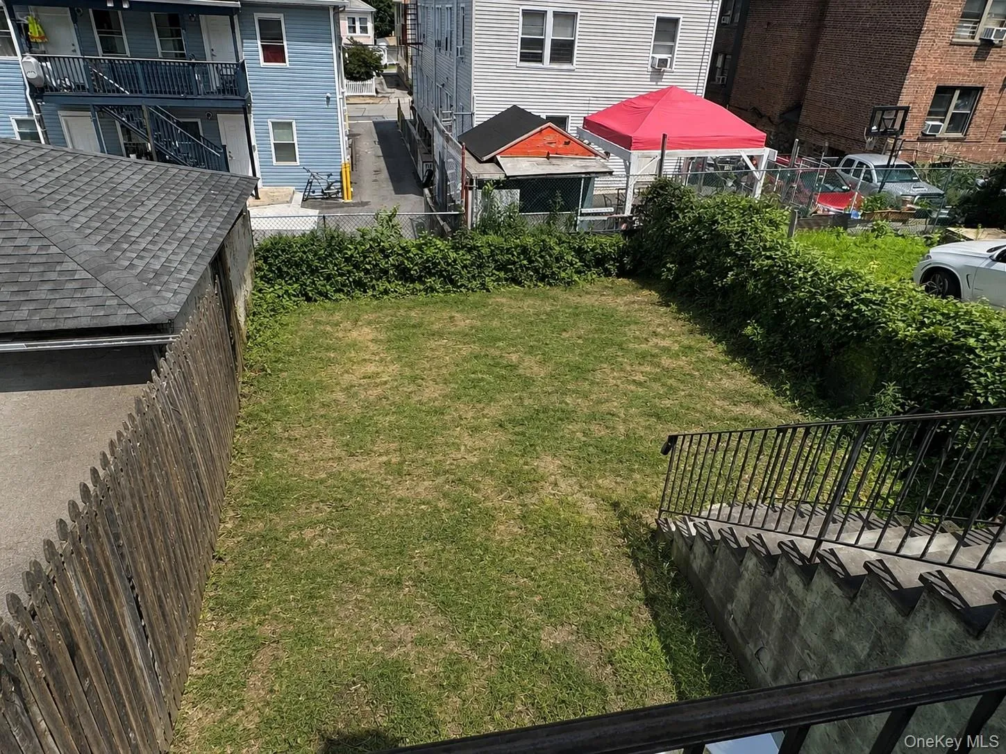 Fenced backyard featuring a grassy lawn, stone steps with metal railings, and mature perimeter hedging Fenced backyard featuring a grassy lawn, stone steps with metal railings, and mature perimeter hedging