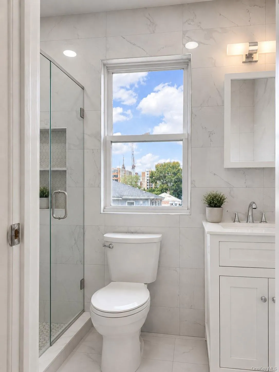Bathroom featuring a glass-enclosed shower with tiled niche, a white vanity with an undermount sink and chrome fixtures, a window, and recessed lighting Bathroom featuring a glass-enclosed shower with tiled niche, a white vanity with an undermount sink and chrome fixtures, a window, and recessed lighting