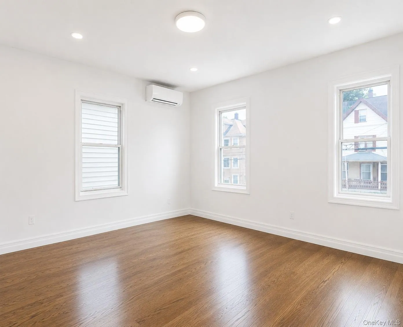 Primary bedroom featuring wood-finish flooring, white baseboards, and three double-hung windows Primary bedroom featuring wood-finish flooring, white baseboards, and three double-hung windows
