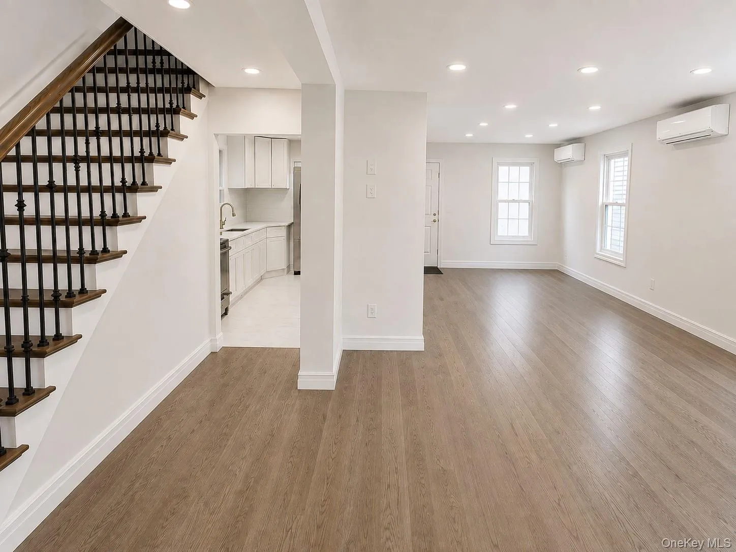Spacious main living area featuring wood-finish flooring, recessed lighting, and white walls Spacious main living area featuring wood-finish flooring, recessed lighting, and white walls