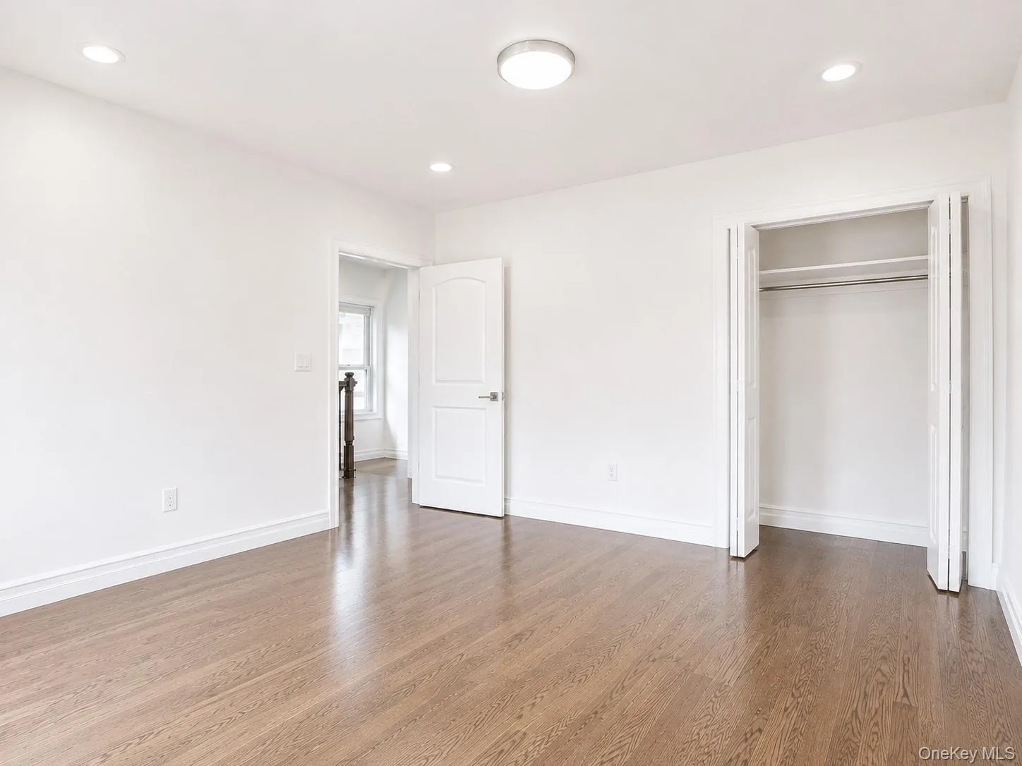 Open concept room featuring wood-finish flooring, white walls, recessed ceiling lights, and a built-in closet with bi-fold doors Open concept room featuring wood-finish flooring, white walls, recessed ceiling lights, and a built-in closet with bi-fold doors