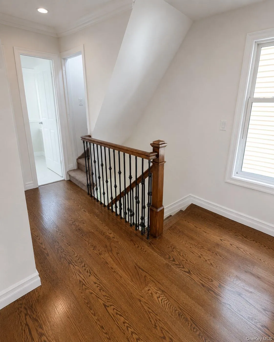 Hardwood flooring throughout the landing, featuring a staircase with carpeted treads, dark wrought iron balusters, and a substantial wood newel post Hardwood flooring throughout the landing, featuring a staircase with carpeted treads, dark wrought iron balusters, and a substantial wood newel post