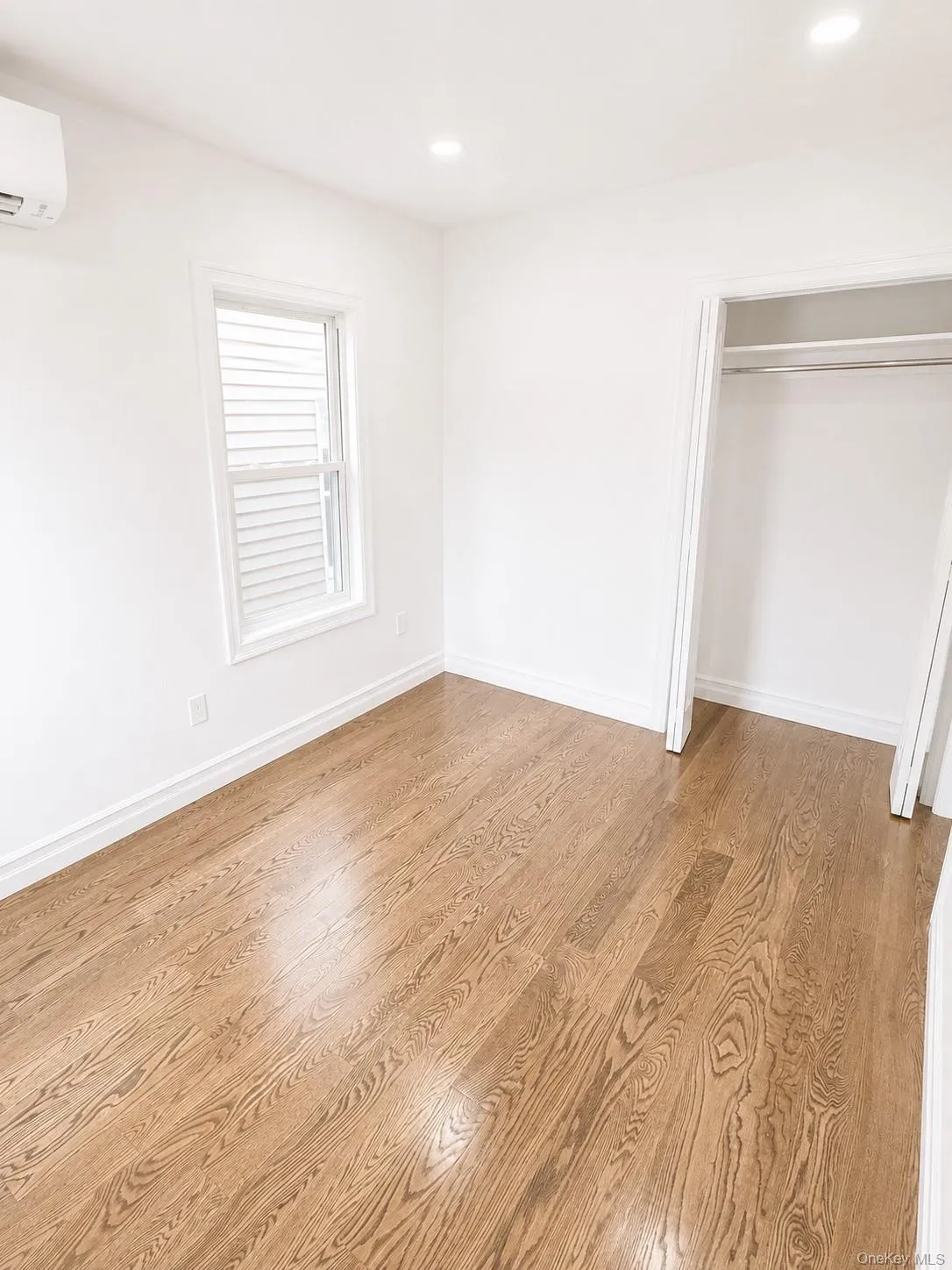 Bedroom with hardwood flooring, recessed lighting, double-hung window with blinds, white trim, and a built-in closet with hanging rod Bedroom with hardwood flooring, recessed lighting, double-hung window with blinds, white trim, and a built-in closet with hanging rod