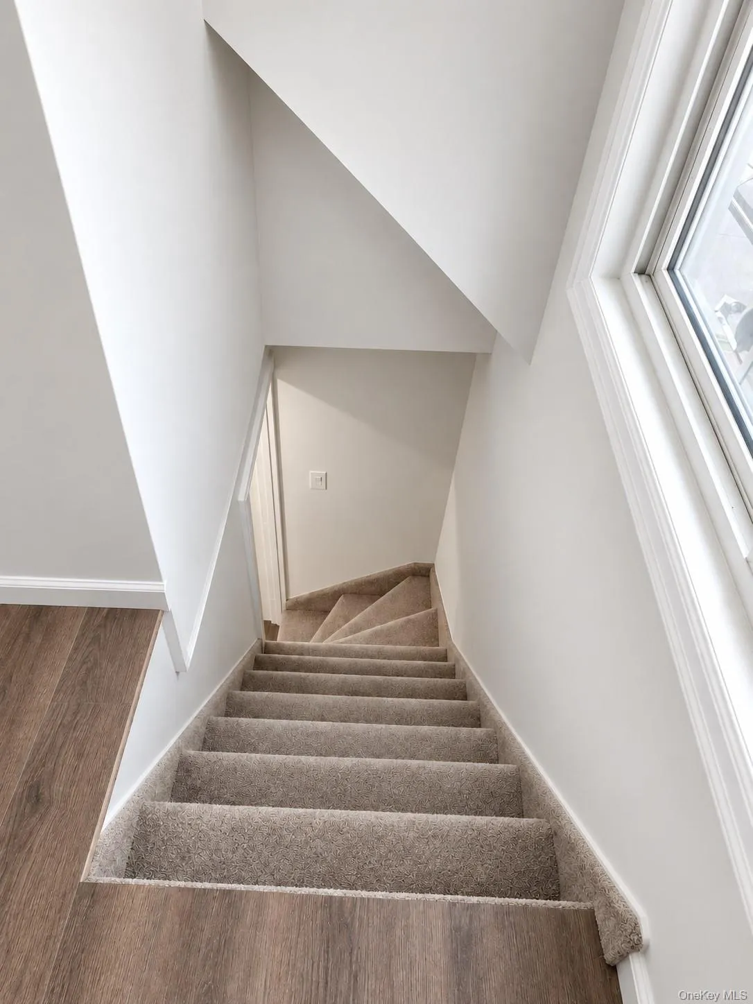 Carpeted staircase with light-colored risers and wood-finish flooring at the base Carpeted staircase with light-colored risers and wood-finish flooring at the base