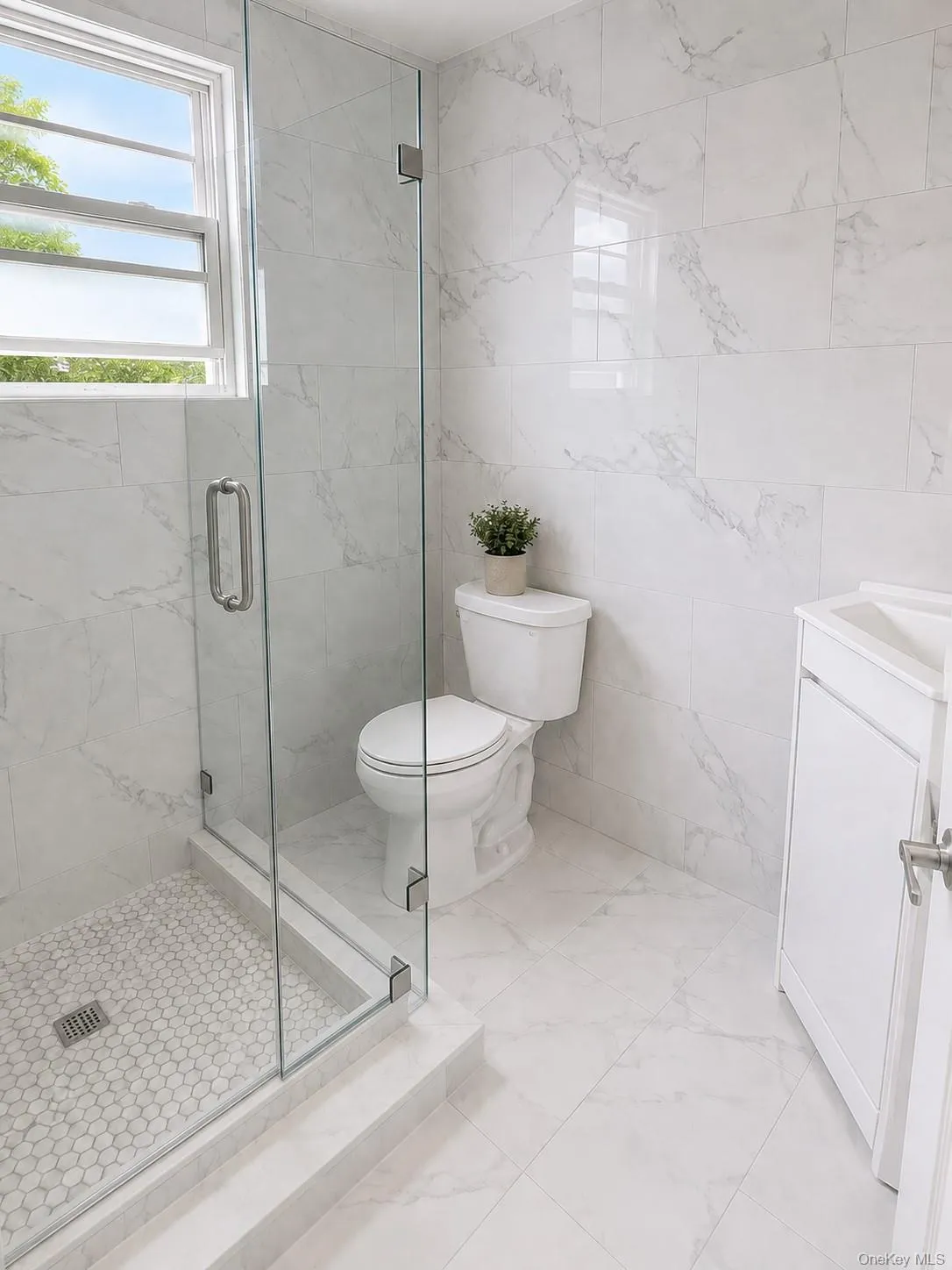 Bathroom featuring a glass-enclosed shower with pebble tile base, large format wall and floor tiling, and a single-door vanity cabinet Bathroom featuring a glass-enclosed shower with pebble tile base, large format wall and floor tiling, and a single-door vanity cabinet