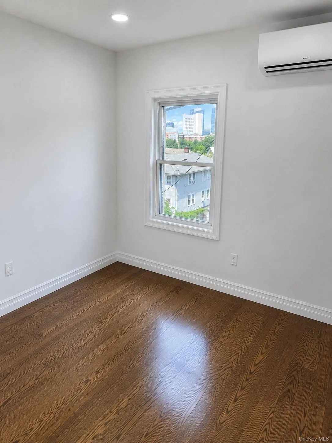 Bedroom featuring rich wood-finish flooring, white baseboards, and a large window with white trim Bedroom featuring rich wood-finish flooring, white baseboards, and a large window with white trim
