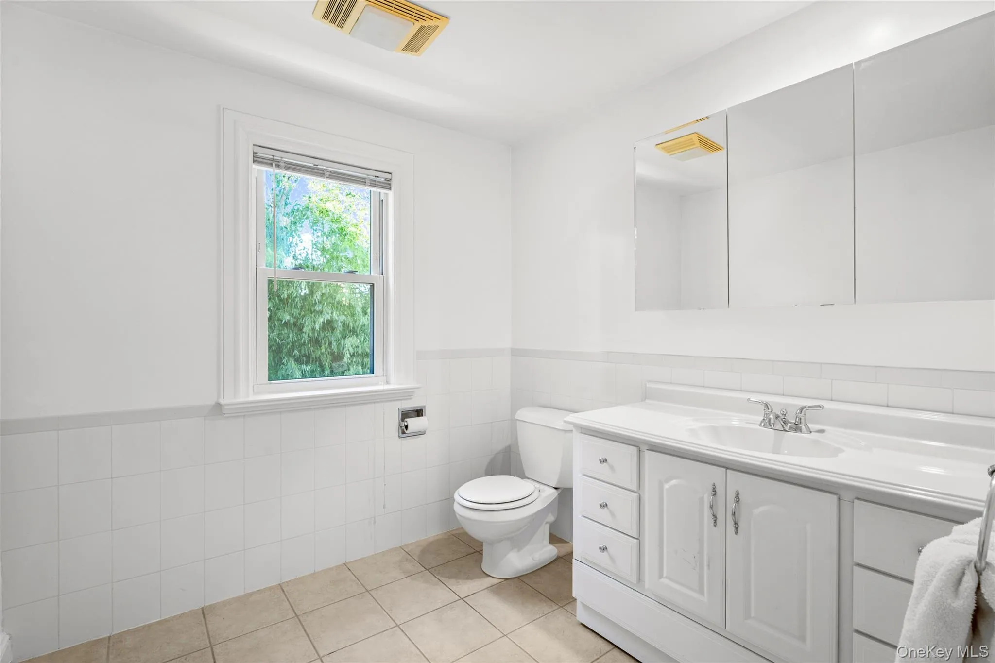 Top floor full bathroom with a wainscoted wall, tile walls, vanity, and light tile patterned floors. Top floor full bathroom with a wainscoted wall, tile walls, vanity, and light tile patterned floors.