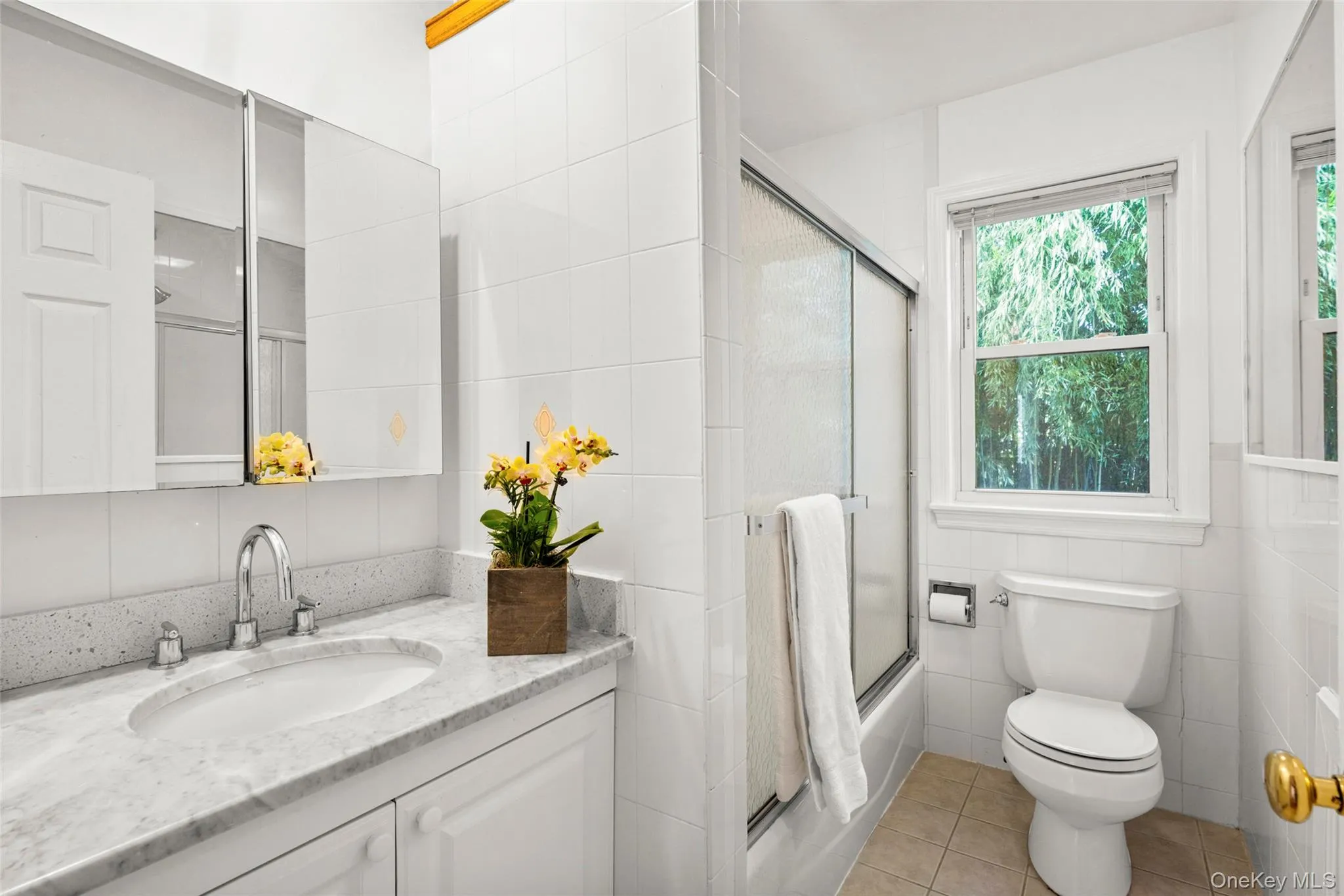 Hall Bathroom featuring tile walls, light tile patterned flooring, vanity, and enclosed tub /shower combo. Hall Bathroom featuring tile walls, light tile patterned flooring, vanity, and enclosed tub /shower combo.