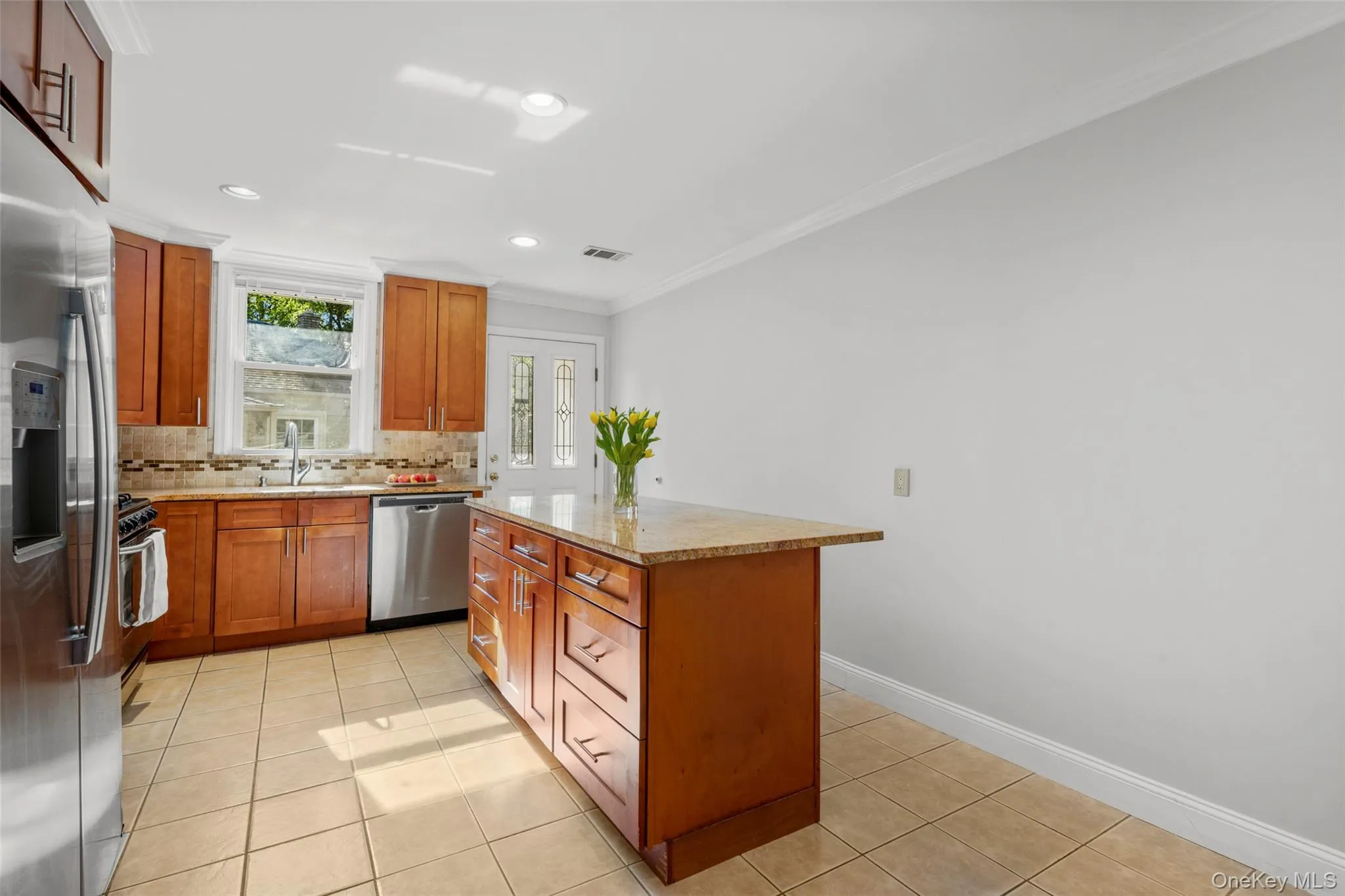 Kitchen featuring plenty cabinetry, backsplash, crown molding, stainless steel appliances, and light tile patterned floors, door to side entrance. Kitchen featuring plenty cabinetry, backsplash, crown molding, stainless steel appliances, and light tile patterned floors, door to side entrance.