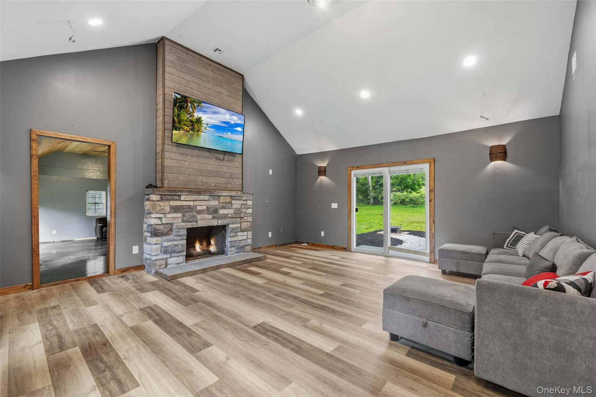 Spacious living area featuring a vaulted ceiling with recessed lighting, vinyl-finish flooring, sliding glass doors, and a stone-faced fireplace with a tile hearth Spacious living area featuring a vaulted ceiling with recessed lighting, vinyl-finish flooring, sliding glass doors, and a stone-faced fireplace with a tile hearth