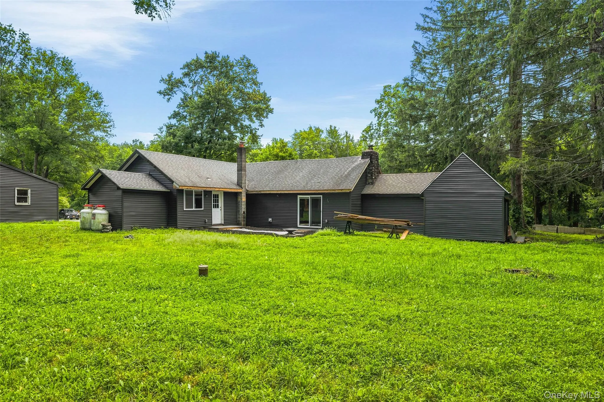 Modern ranch home set on expansive grounds featuring a dramatic gabled roofline, dark exterior siding, and multiple connected structures Modern ranch home set on expansive grounds featuring a dramatic gabled roofline, dark exterior siding, and multiple connected structures