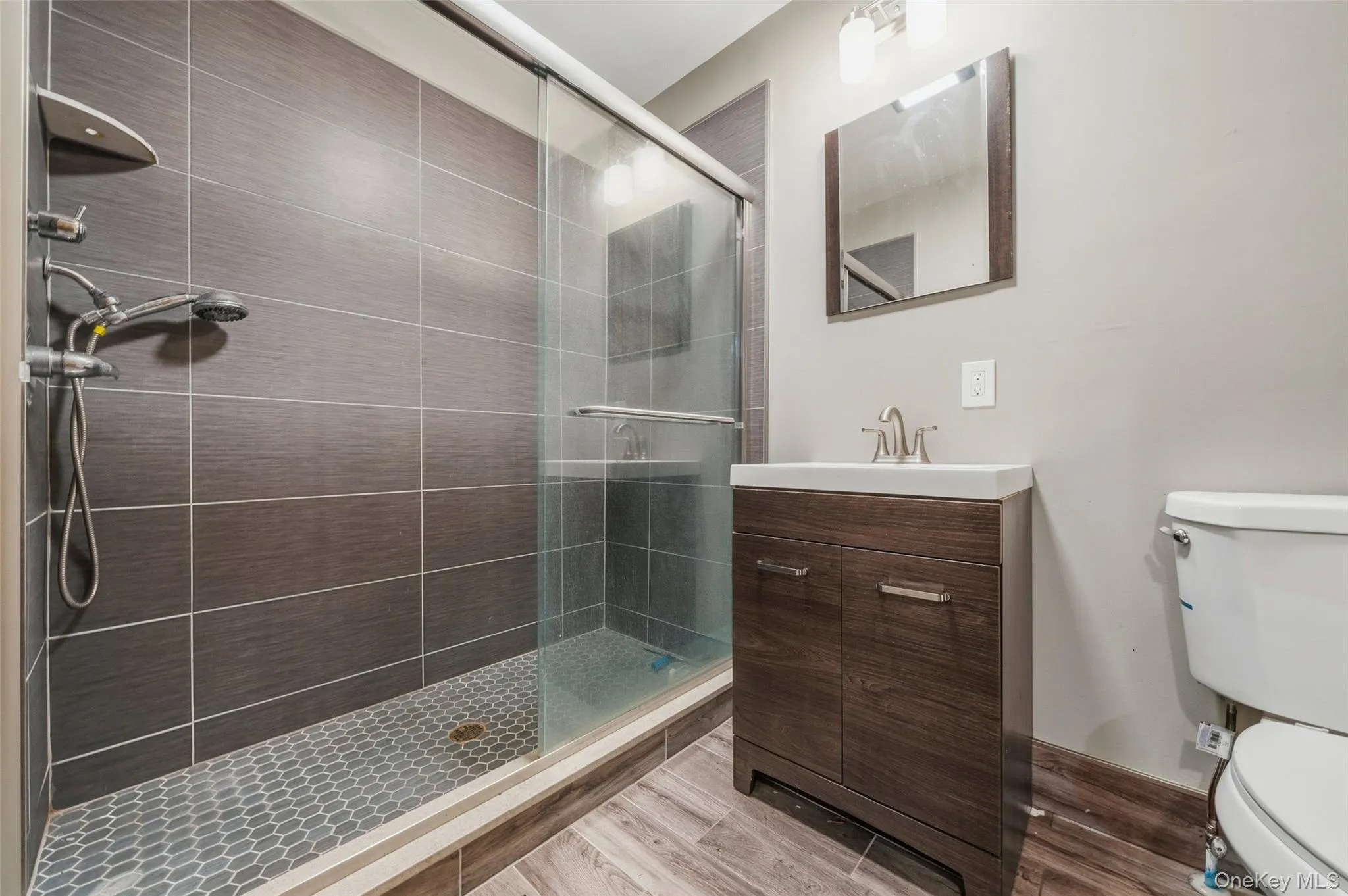 Modern full bathroom featuring a frameless glass-enclosed shower with dual showerheads, linear tile detailing, and a mosaic tile floor Modern full bathroom featuring a frameless glass-enclosed shower with dual showerheads, linear tile detailing, and a mosaic tile floor