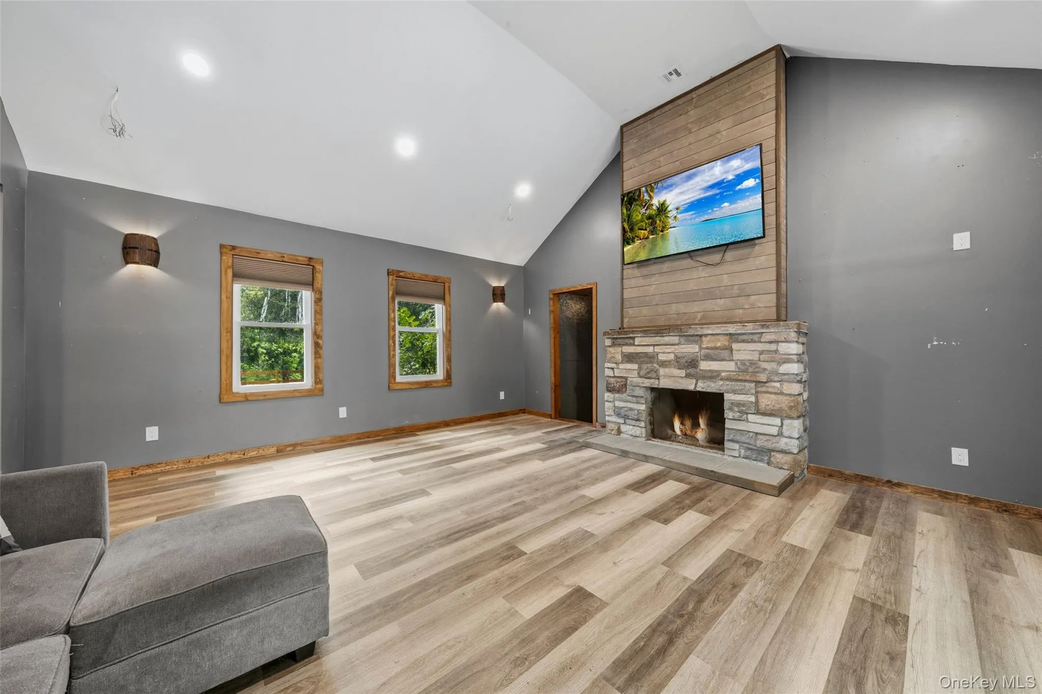 Spacious living area featuring a vaulted ceiling with recessed lighting, vinyl-finish flooring, and a stone-faced fireplace with a tile hearth Spacious living area featuring a vaulted ceiling with recessed lighting, vinyl-finish flooring, and a stone-faced fireplace with a tile hearth
