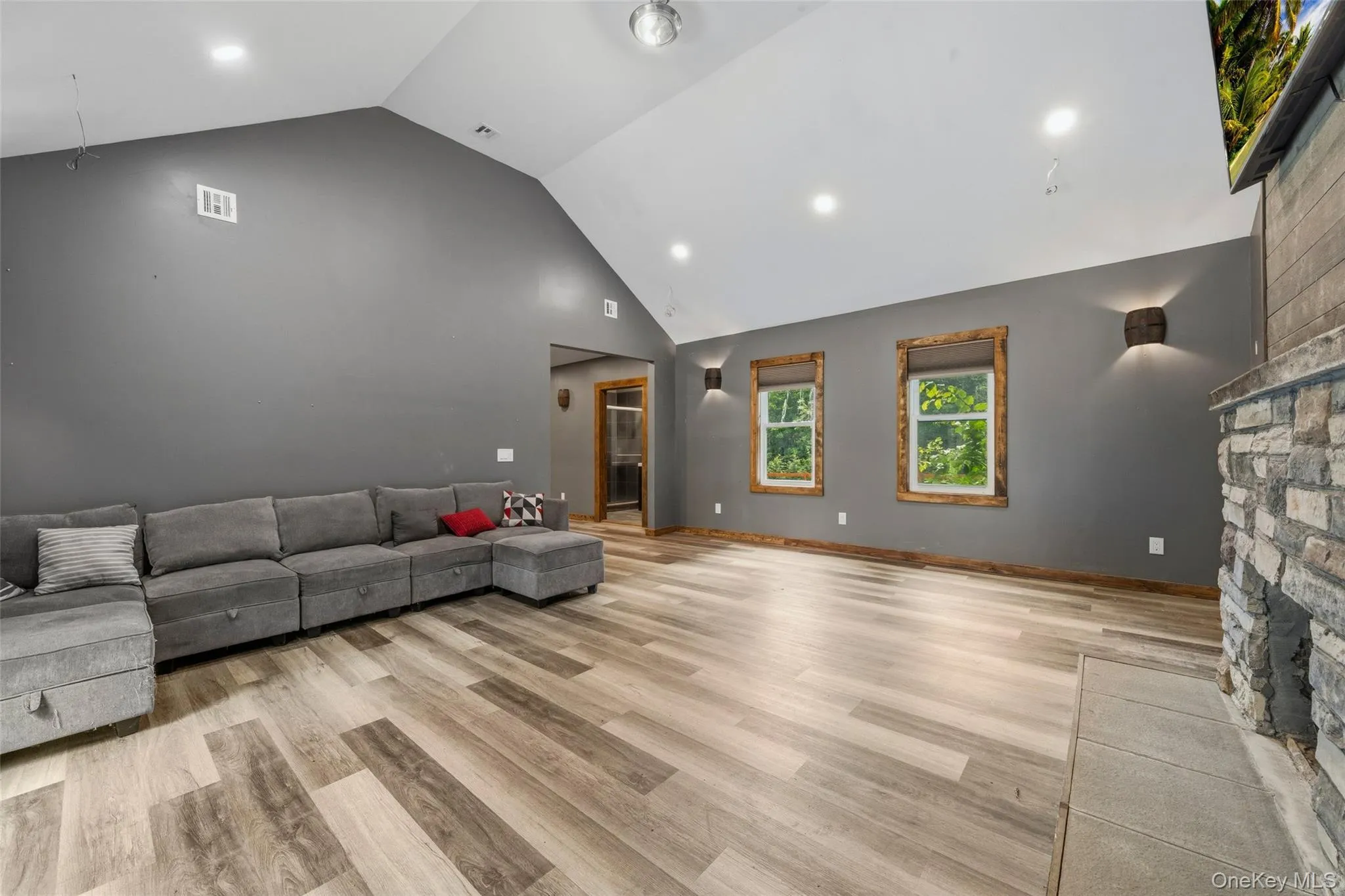 Spacious living area featuring a vaulted ceiling with recessed lighting, vinyl-finish flooring, and a stone-faced fireplace with a tile hearth Spacious living area featuring a vaulted ceiling with recessed lighting, vinyl-finish flooring, and a stone-faced fireplace with a tile hearth