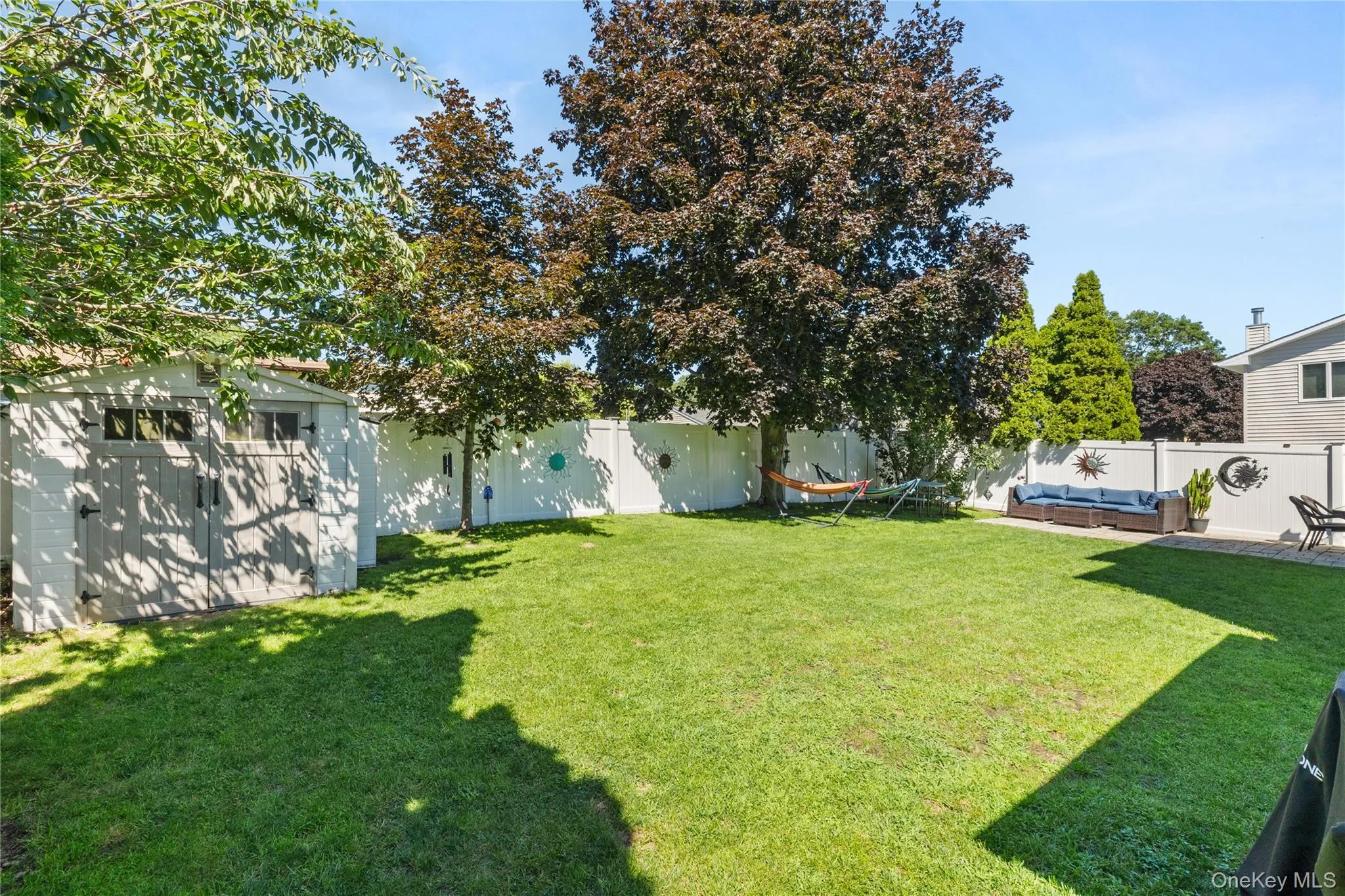 Expansive backyard with a manicured lawn, established trees, privacy fencing, a storage shed, and a paved patio area Expansive backyard with a manicured lawn, established trees, privacy fencing, a storage shed, and a paved patio area
