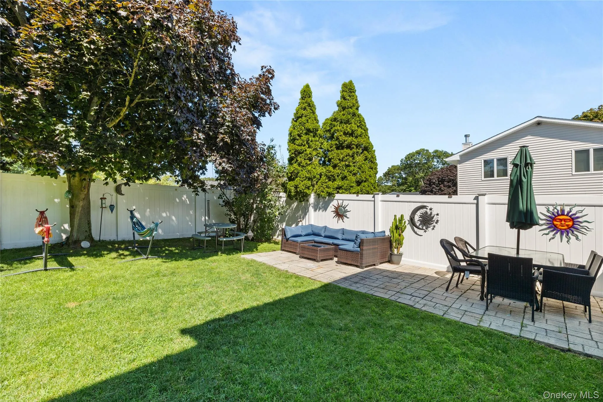 Expansive backyard featuring a manicured lawn, a large shade tree, and a white privacy fence Expansive backyard featuring a manicured lawn, a large shade tree, and a white privacy fence