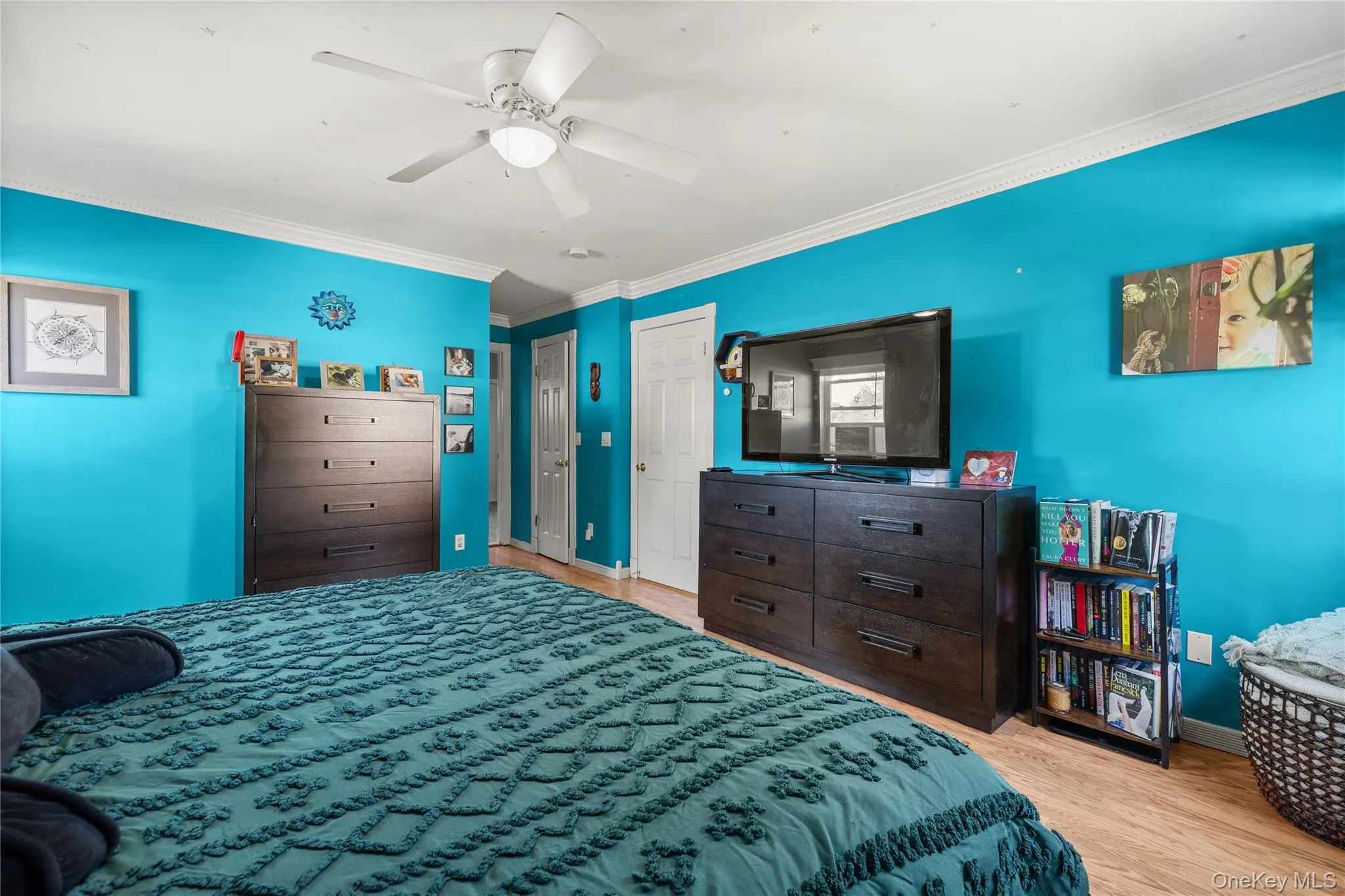 Spacious room featuring wood-finish flooring, a ceiling fan, crown molding, and two white paneled doors Spacious room featuring wood-finish flooring, a ceiling fan, crown molding, and two white paneled doors