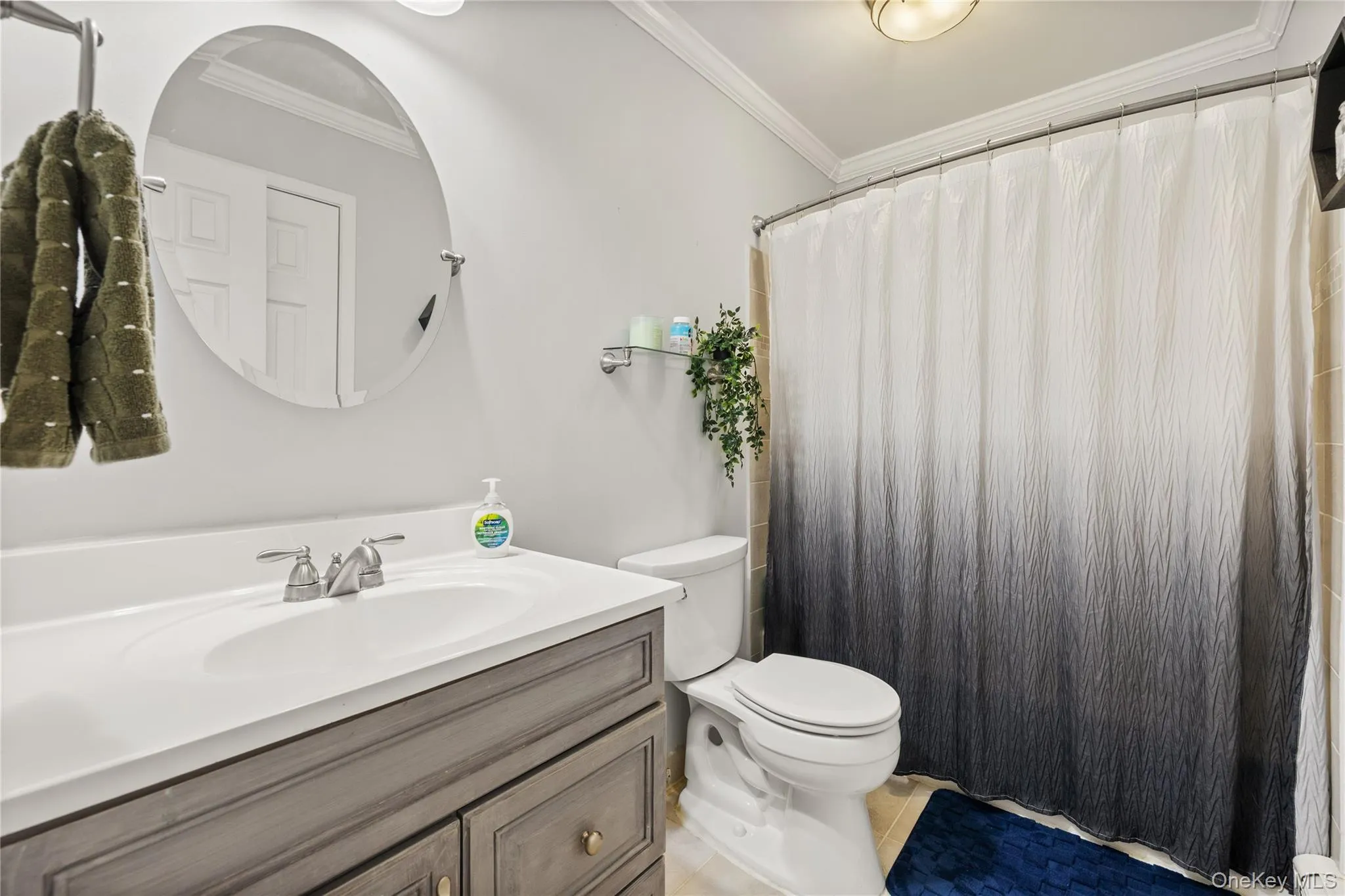 Bathroom featuring a vanity with a white countertop and a gray wood-finish cabinet, a round wall-mounted mirror, and a full shower with a tub Bathroom featuring a vanity with a white countertop and a gray wood-finish cabinet, a round wall-mounted mirror, and a full shower with a tub