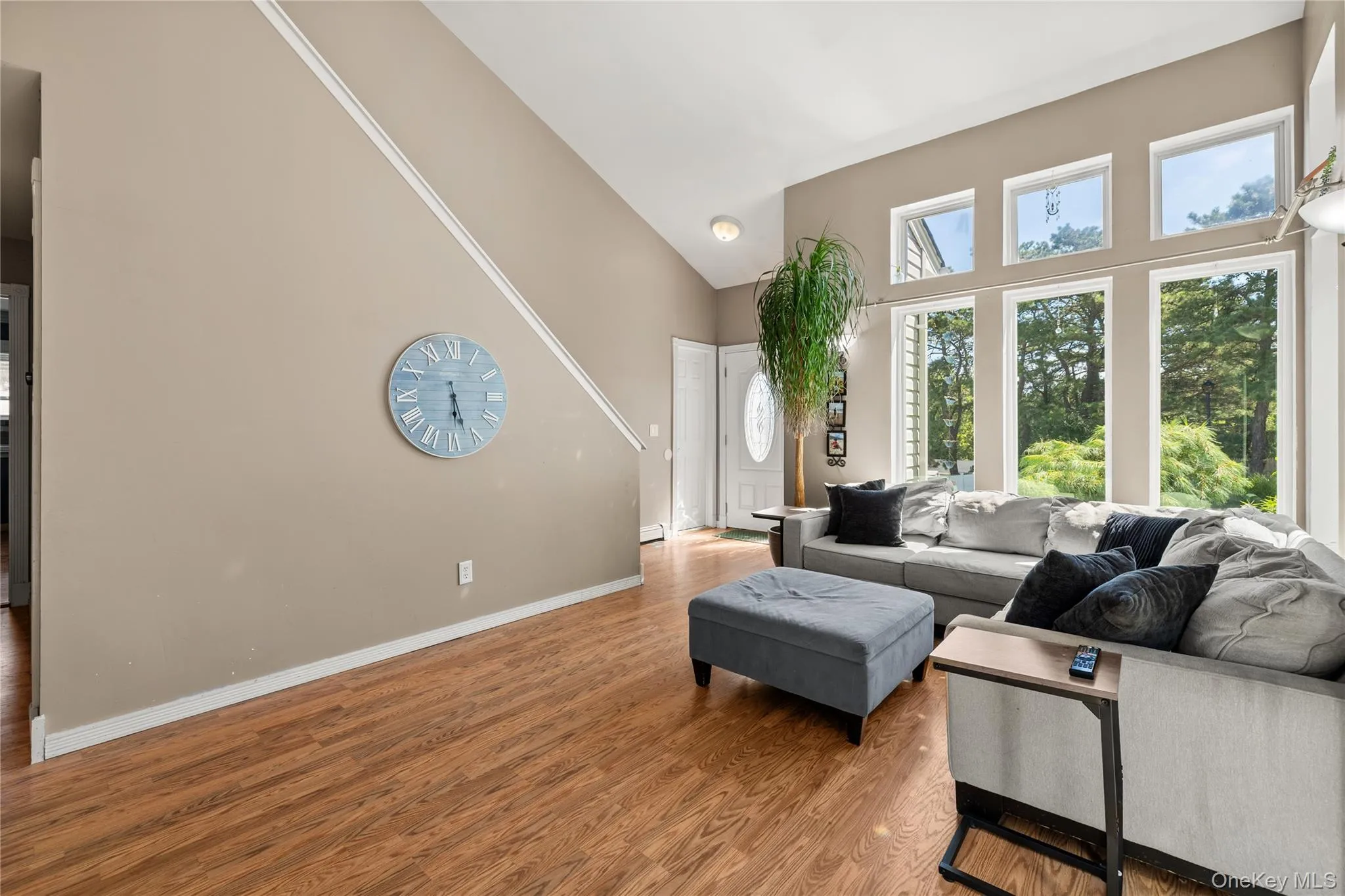 Vaulted ceiling living area featuring wood-finish flooring, a wall of multiple windows, and a white paneled front door Vaulted ceiling living area featuring wood-finish flooring, a wall of multiple windows, and a white paneled front door
