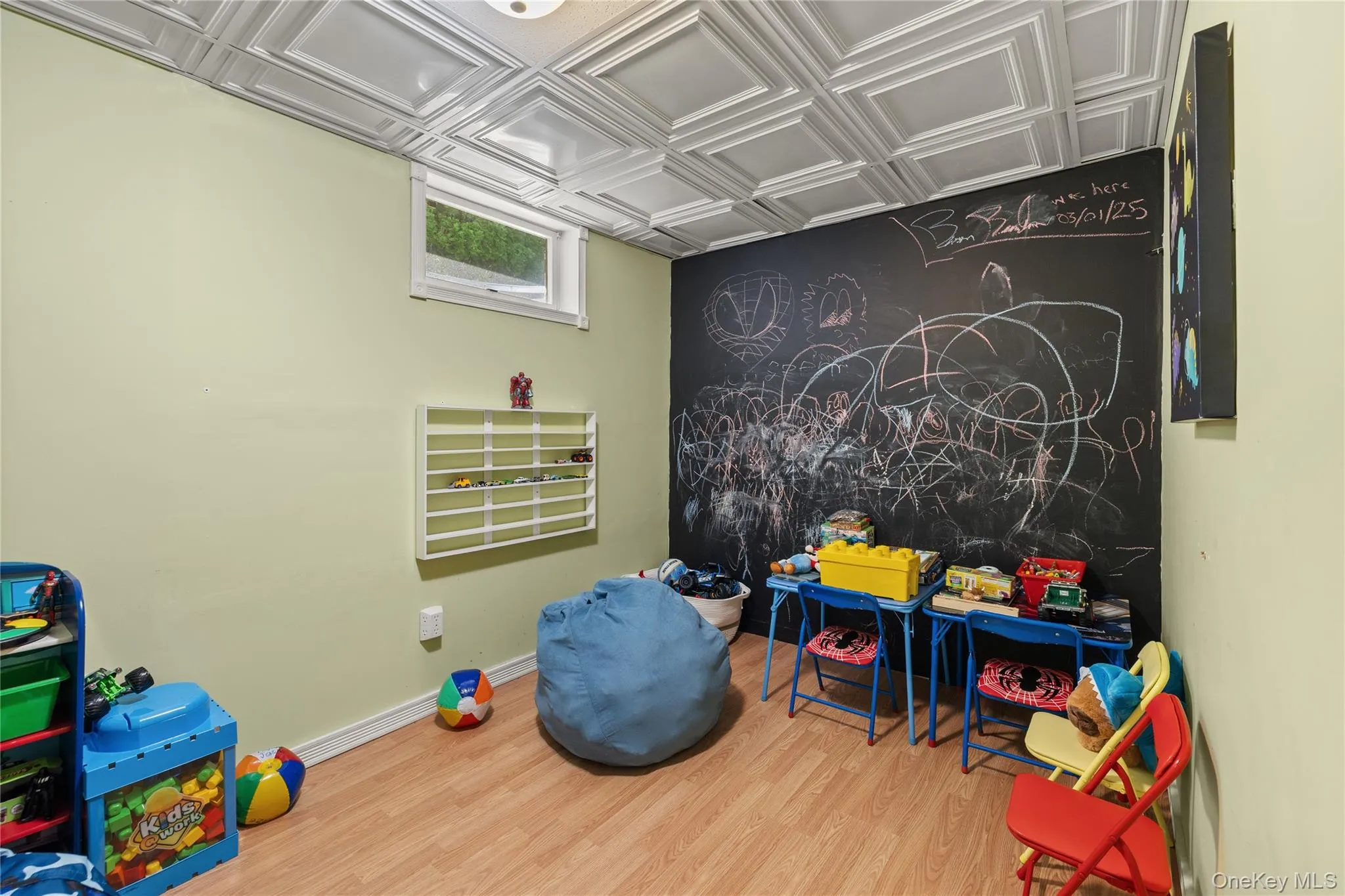 Room featuring wood-finish flooring, a decorative ceiling with square panels, and a chalkboard wall Room featuring wood-finish flooring, a decorative ceiling with square panels, and a chalkboard wall
