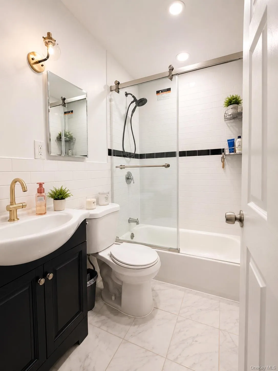 Modern bathroom featuring a sleek black vanity with brass hardware and vessel sink, white subway tile walls, and a frameless glass shower enclosure with a black tile accent stripe Modern bathroom featuring a sleek black vanity with brass hardware and vessel sink, white subway tile walls, and a frameless glass shower enclosure with a black tile accent stripe