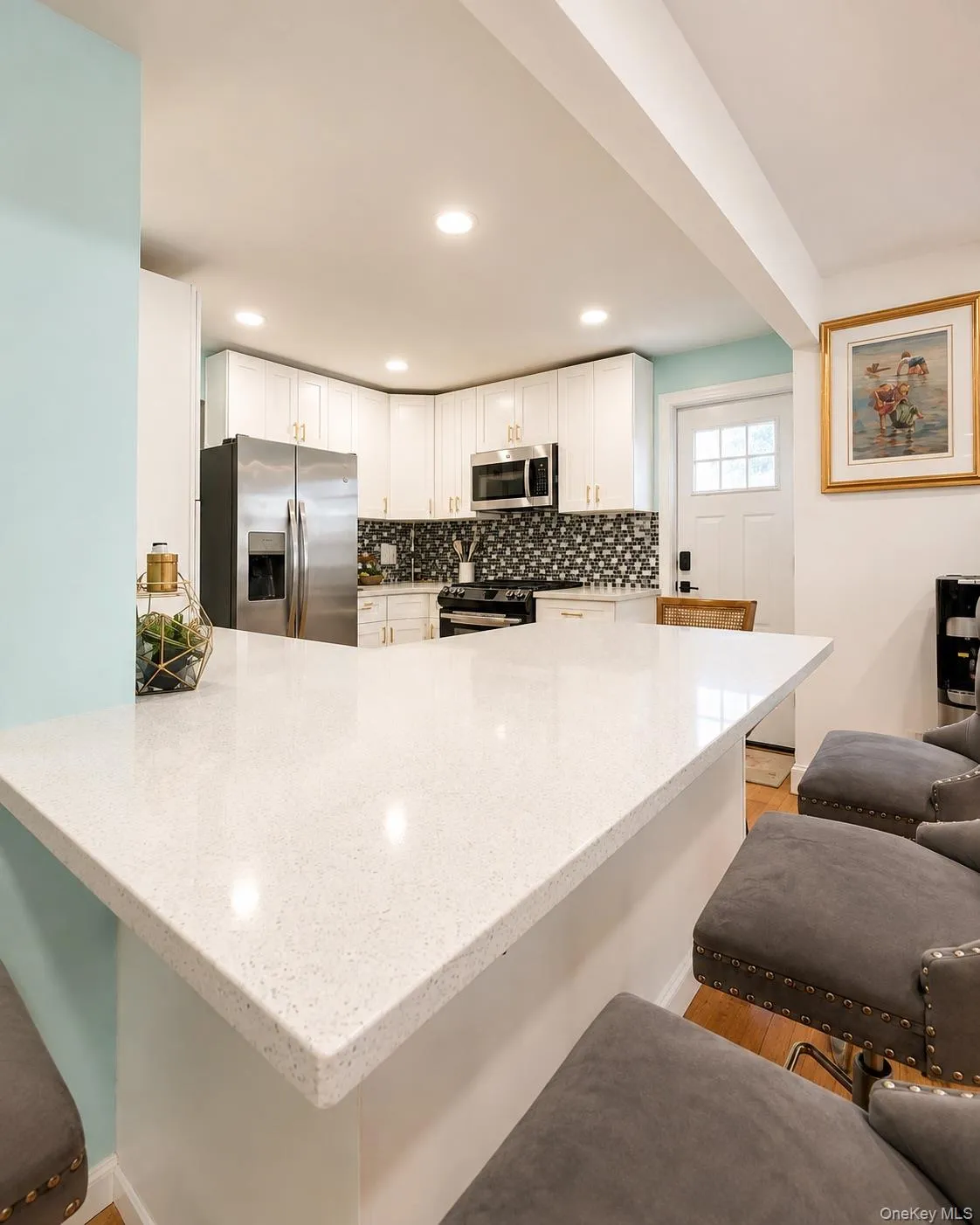 Kitchen featuring a large light-toned island with ample counter space, white cabinetry, stainless steel appliances, recessed ceiling lighting, and a geometric pattern backsplash Kitchen featuring a large light-toned island with ample counter space, white cabinetry, stainless steel appliances, recessed ceiling lighting, and a geometric pattern backsplash