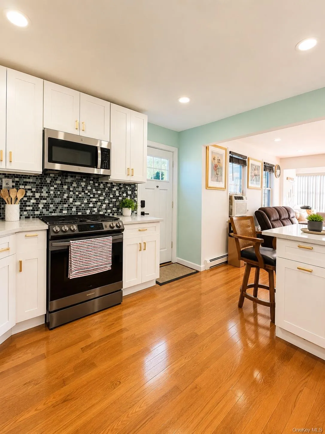 Bright, updated kitchen featuring white cabinetry with brass hardware, black gas range with tile backsplash, stainless steel microwave, and ample counter space Bright, updated kitchen featuring white cabinetry with brass hardware, black gas range with tile backsplash, stainless steel microwave, and ample counter space