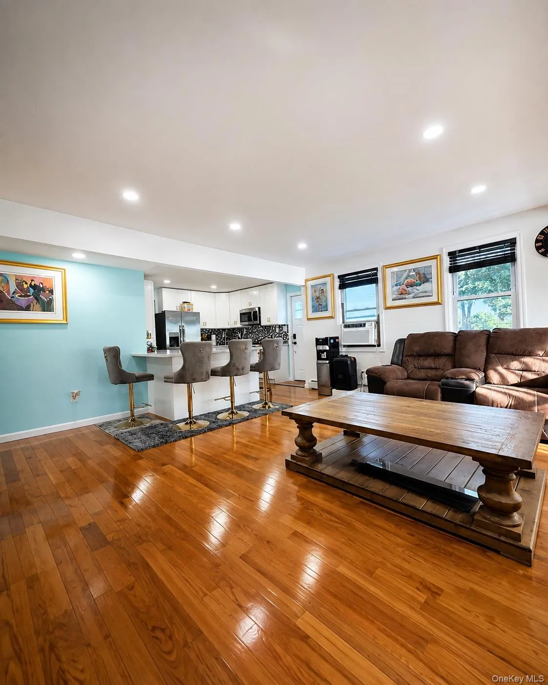 Spacious open-concept living area featuring rich wood-finish flooring throughout, recessed ceiling lighting, and a turquoise accent wall Spacious open-concept living area featuring rich wood-finish flooring throughout, recessed ceiling lighting, and a turquoise accent wall