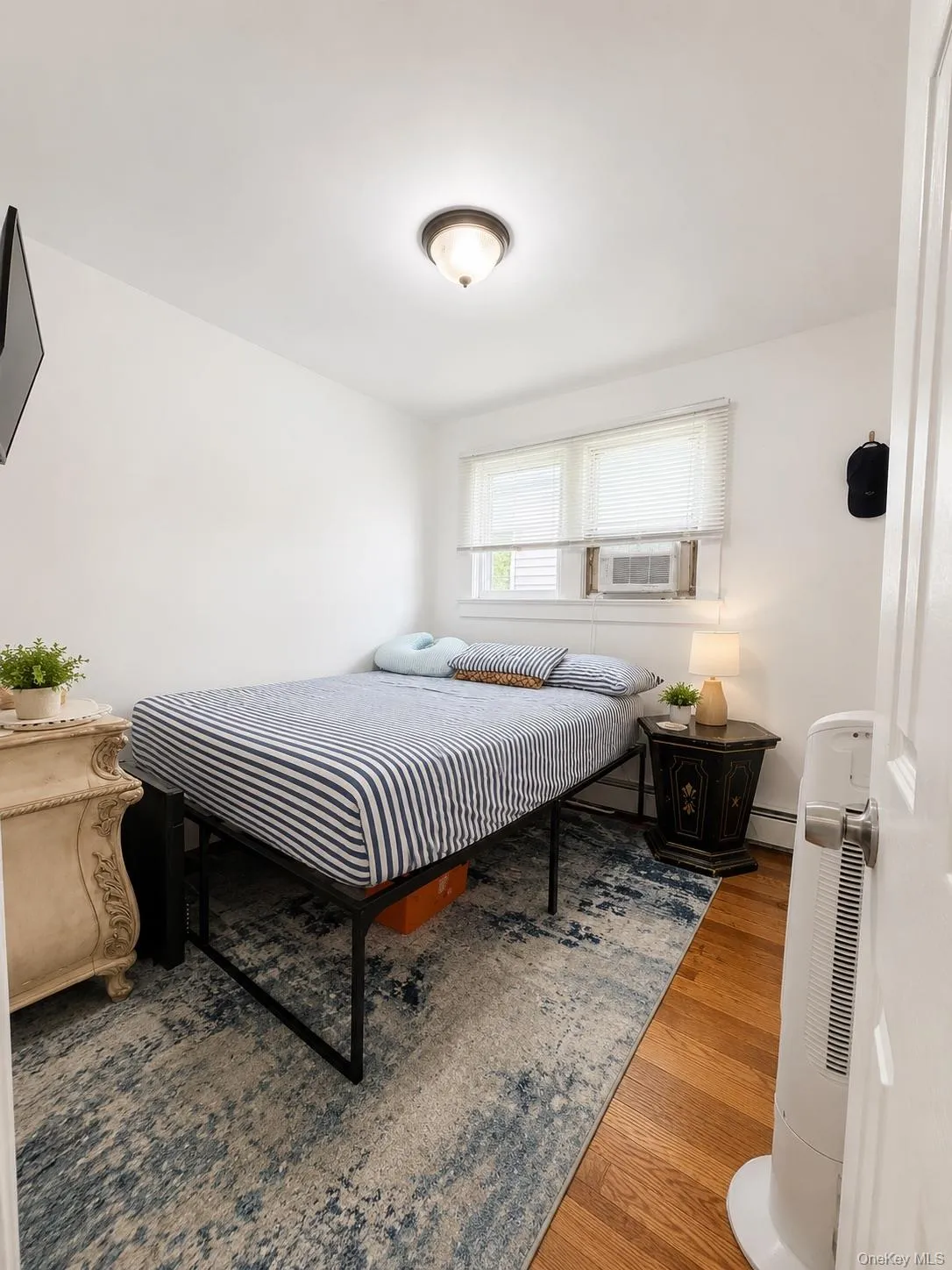 Cozy bedroom featuring hardwood flooring, a striped bedding ensemble, and ample natural light from a multi-pane window Cozy bedroom featuring hardwood flooring, a striped bedding ensemble, and ample natural light from a multi-pane window