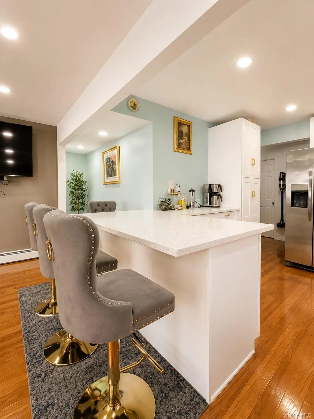 Modern kitchen island featuring a white quartz countertop, integrated seating for two with upholstered gray chairs and brass-finished legs, and white cabinetry Modern kitchen island featuring a white quartz countertop, integrated seating for two with upholstered gray chairs and brass-finished legs, and white cabinetry