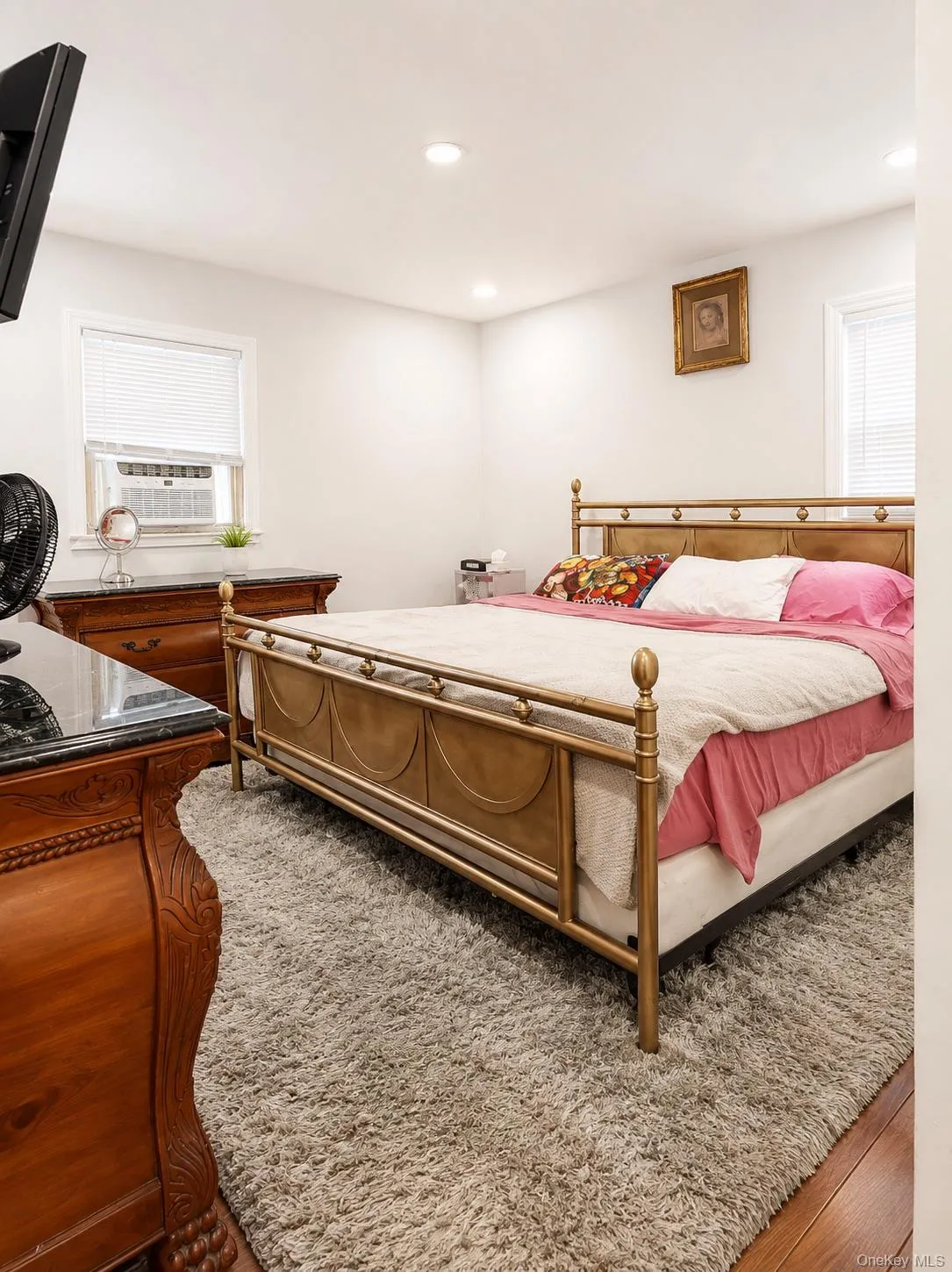 Spacious bedroom featuring a brass and wood bed frame, neutral bedding, plush area rug, and recessed ceiling lighting Spacious bedroom featuring a brass and wood bed frame, neutral bedding, plush area rug, and recessed ceiling lighting