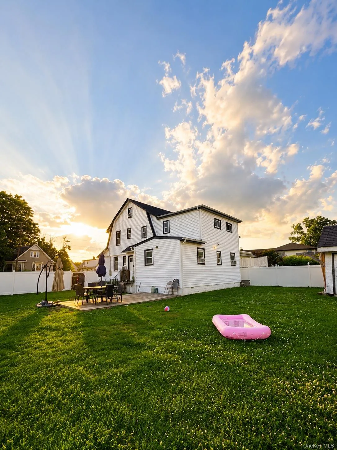Expansive backyard with a manicured lawn, concrete patio, and white vinyl perimeter fencing Expansive backyard with a manicured lawn, concrete patio, and white vinyl perimeter fencing