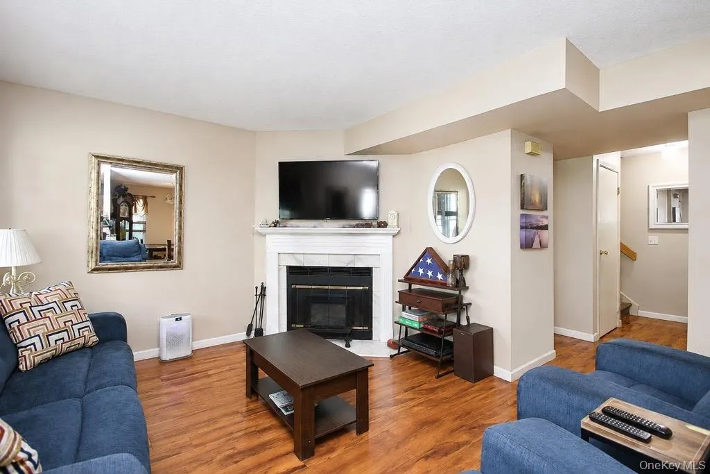 Living area featuring wood-finish flooring, a white mantel fireplace with a black insert, and neutral painted walls Living area featuring wood-finish flooring, a white mantel fireplace with a black insert, and neutral painted walls