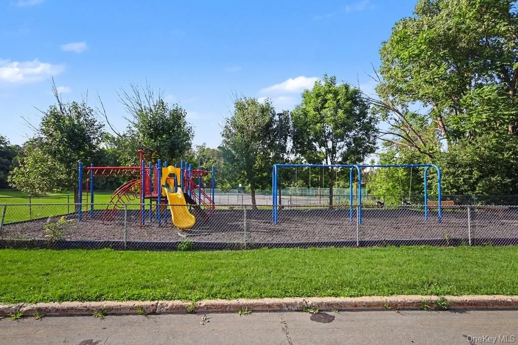 Outdoor recreation area featuring a colorful playground structure, swing set, and chain-link fencing Outdoor recreation area featuring a colorful playground structure, swing set, and chain-link fencing