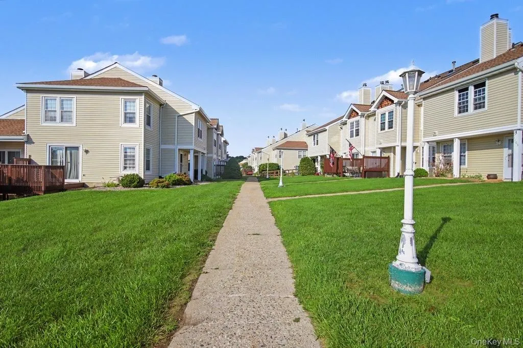 Manicured lawn with a paved pathway flanked by townhomes featuring light-colored siding, brown roofing, and individual rear decks Manicured lawn with a paved pathway flanked by townhomes featuring light-colored siding, brown roofing, and individual rear decks