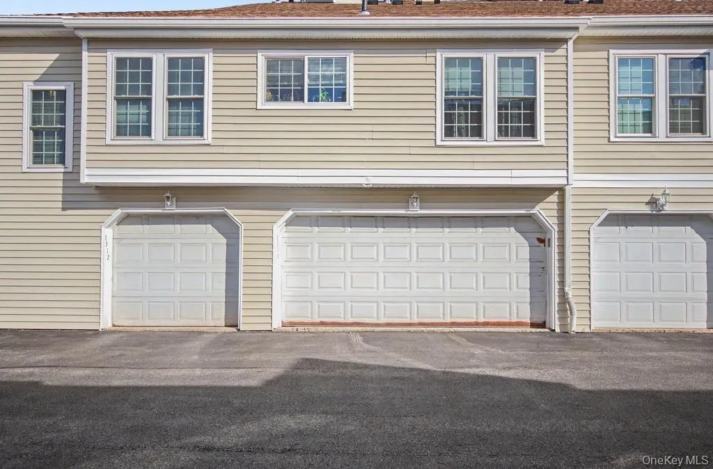 Exterior featuring light-colored horizontal siding, multiple white-framed windows with grilles, and three garage doors with panel detailing Exterior featuring light-colored horizontal siding, multiple white-framed windows with grilles, and three garage doors with panel detailing