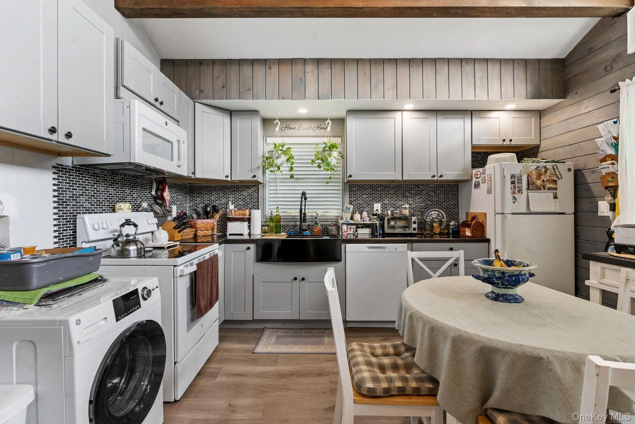 Kitchen with washer / dryer, light wood-style flooring, white appliances, dark countertops, and beamed ceiling Kitchen with washer / dryer, light wood-style flooring, white appliances, dark countertops, and beamed ceiling