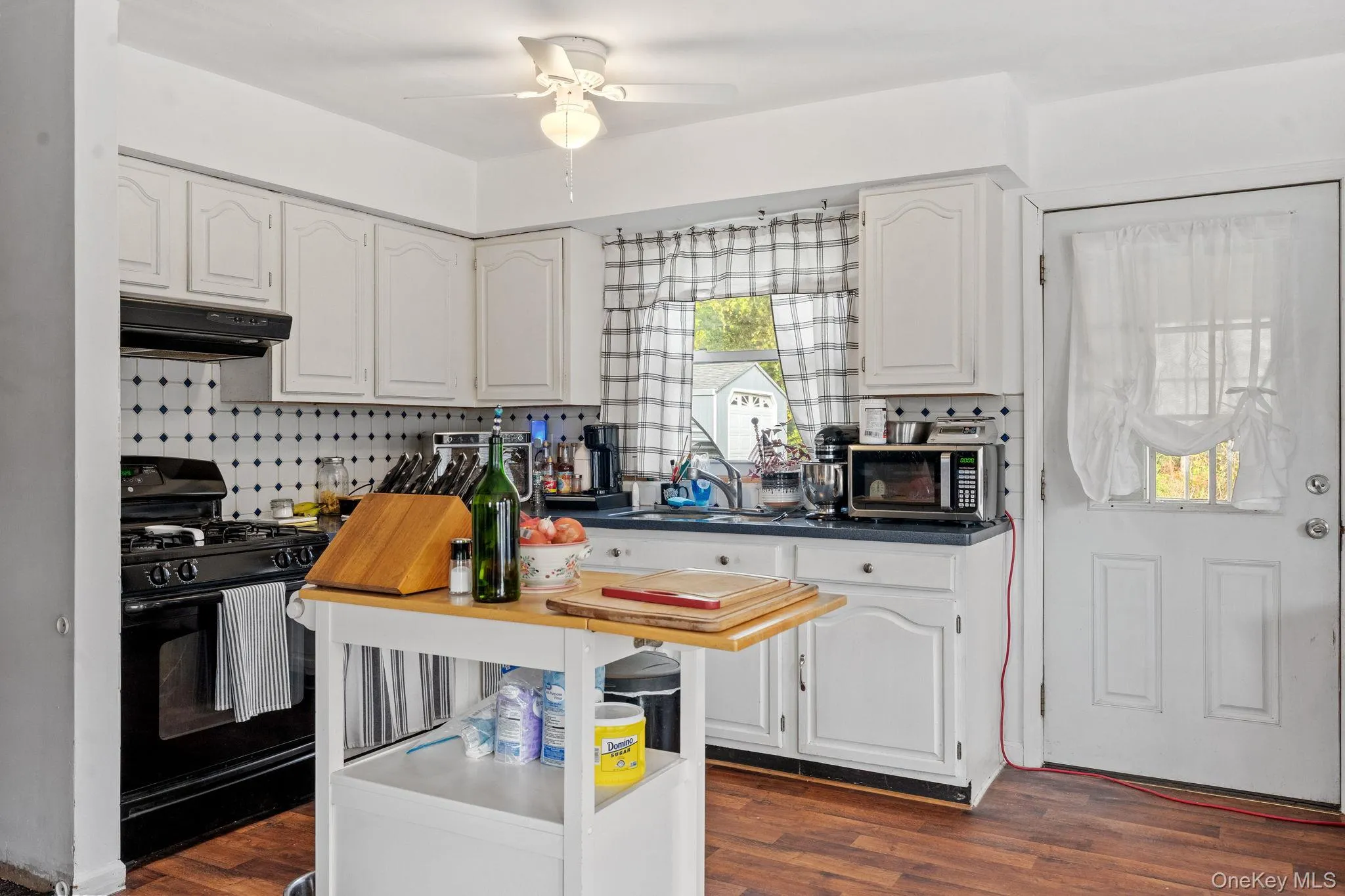 Kitchen featuring black range with gas stovetop, dark countertops, decorative backsplash, and white cabinets Kitchen featuring black range with gas stovetop, dark countertops, decorative backsplash, and white cabinets
