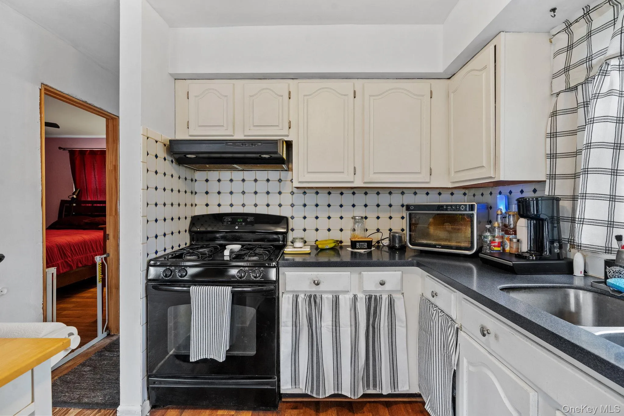 Kitchen featuring backsplash, gas stove, dark countertops, white cabinetry, and dark wood-style floors Kitchen featuring backsplash, gas stove, dark countertops, white cabinetry, and dark wood-style floors