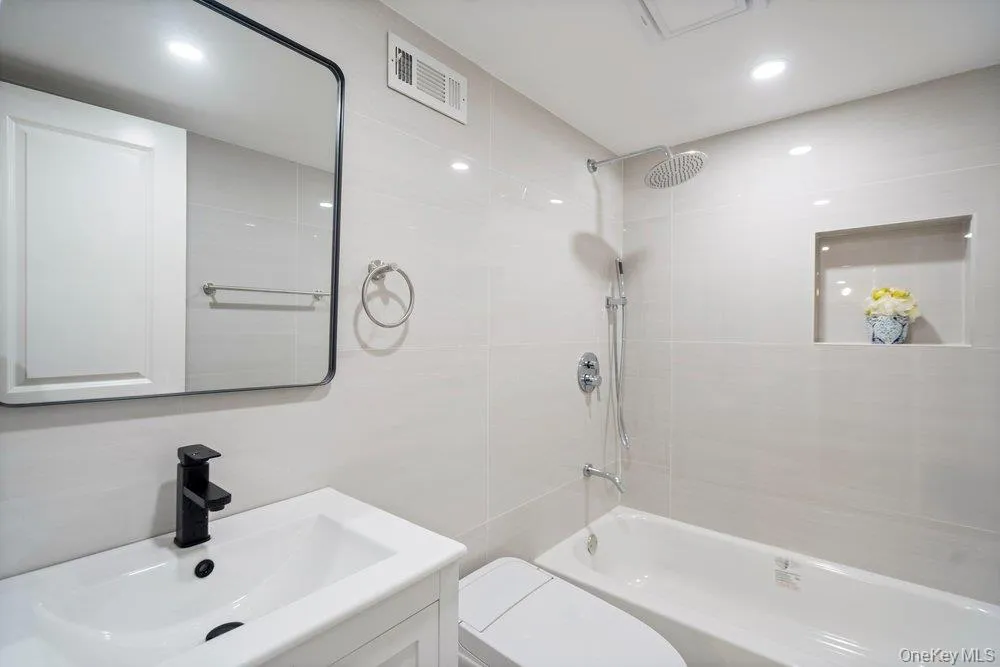 Bathroom featuring a rectangular black-framed mirror, white vanity with integrated sink and matte black faucet, and a bathtub with a rain shower head and handheld sprayer Bathroom featuring a rectangular black-framed mirror, white vanity with integrated sink and matte black faucet, and a bathtub with a rain shower head and handheld sprayer